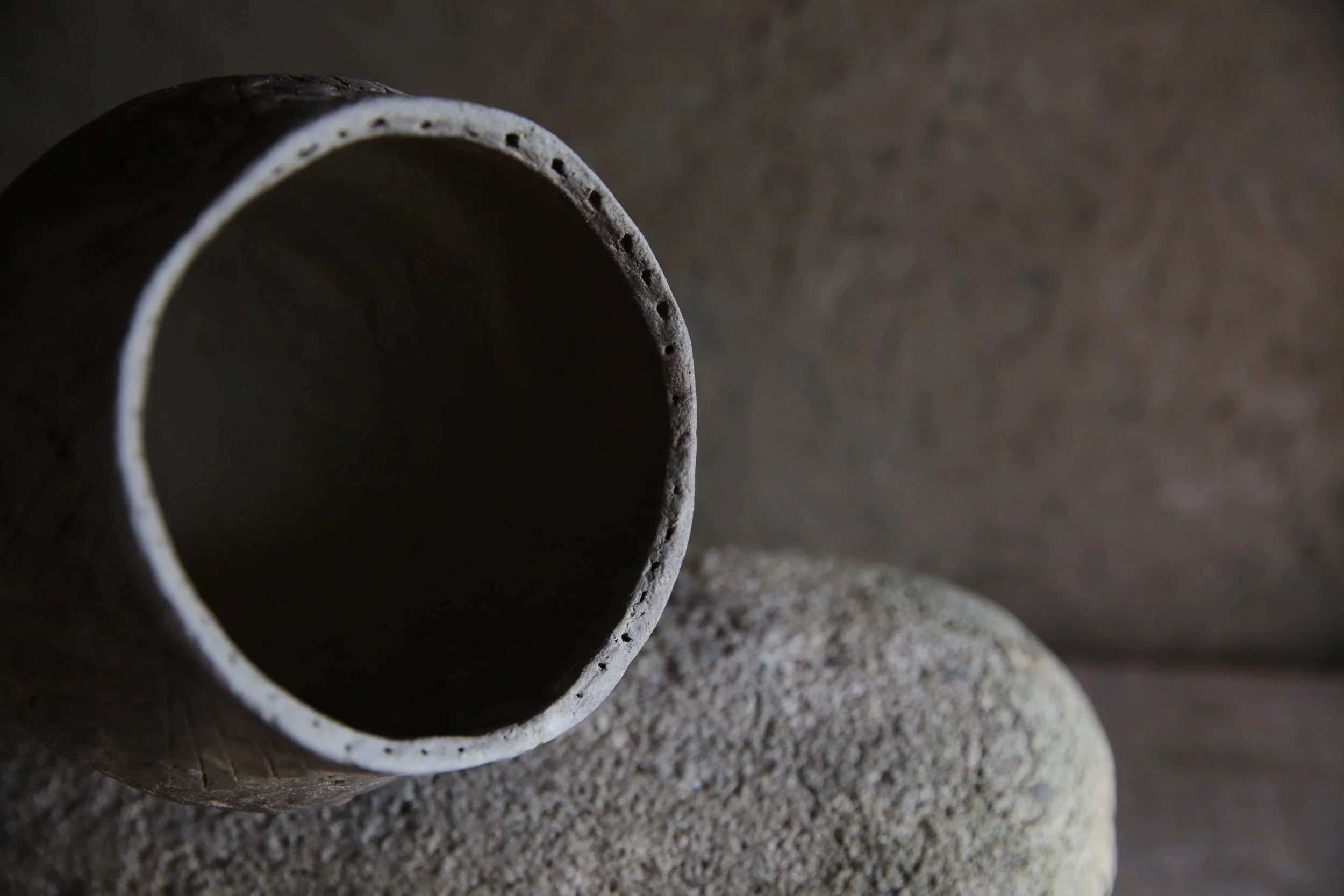 Close-up of a ceramic or clay pipe resting on a textured stone surface with a blurred neutral background.