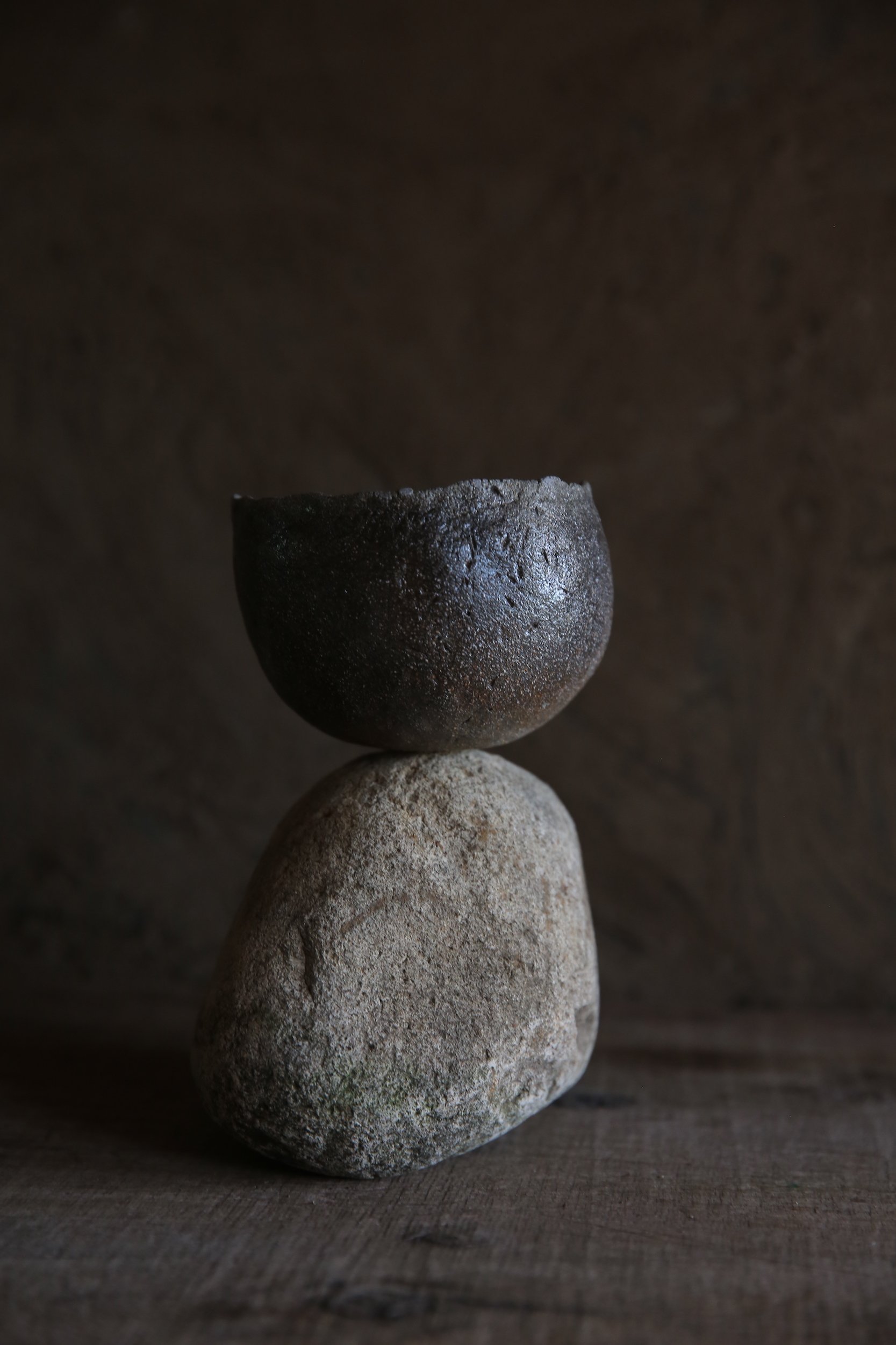 Two stacked stones with a dark, textured bowl on top, set against a dark background.