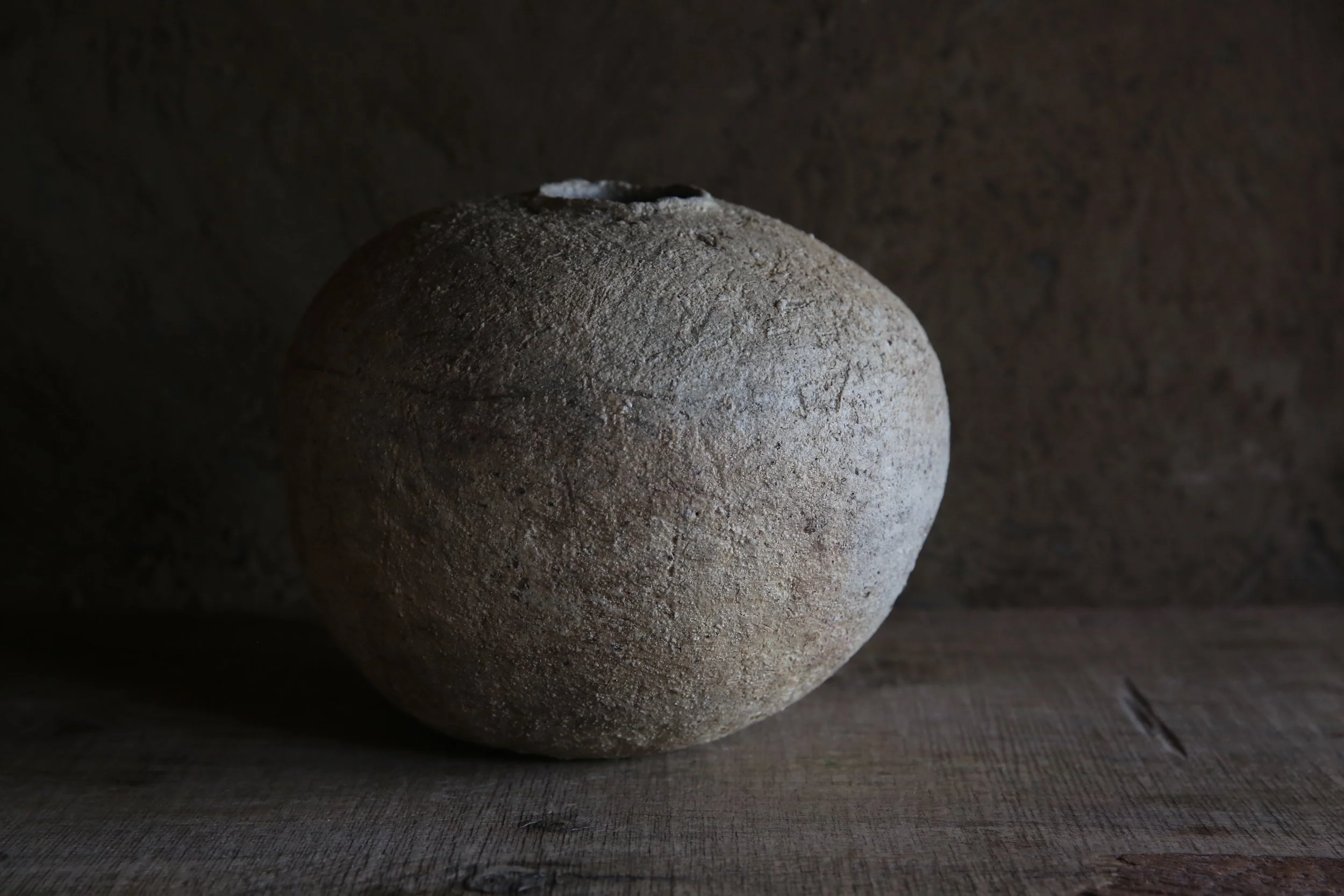 A large, textured stone spherical object on a wooden surface against a dark background.