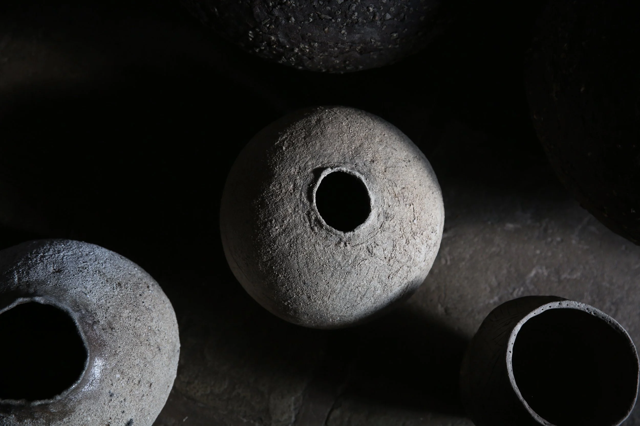Close-up of several old, dusty, stone or clay pipes or vessels with round openings, set against a dark background.