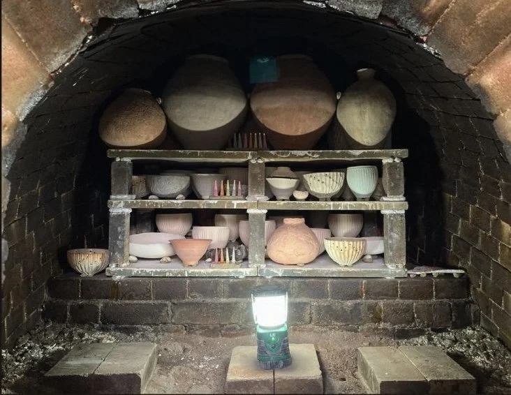 Shelves of unglazed, unfinished clay pottery in a brick kiln with a lamp on the floor.