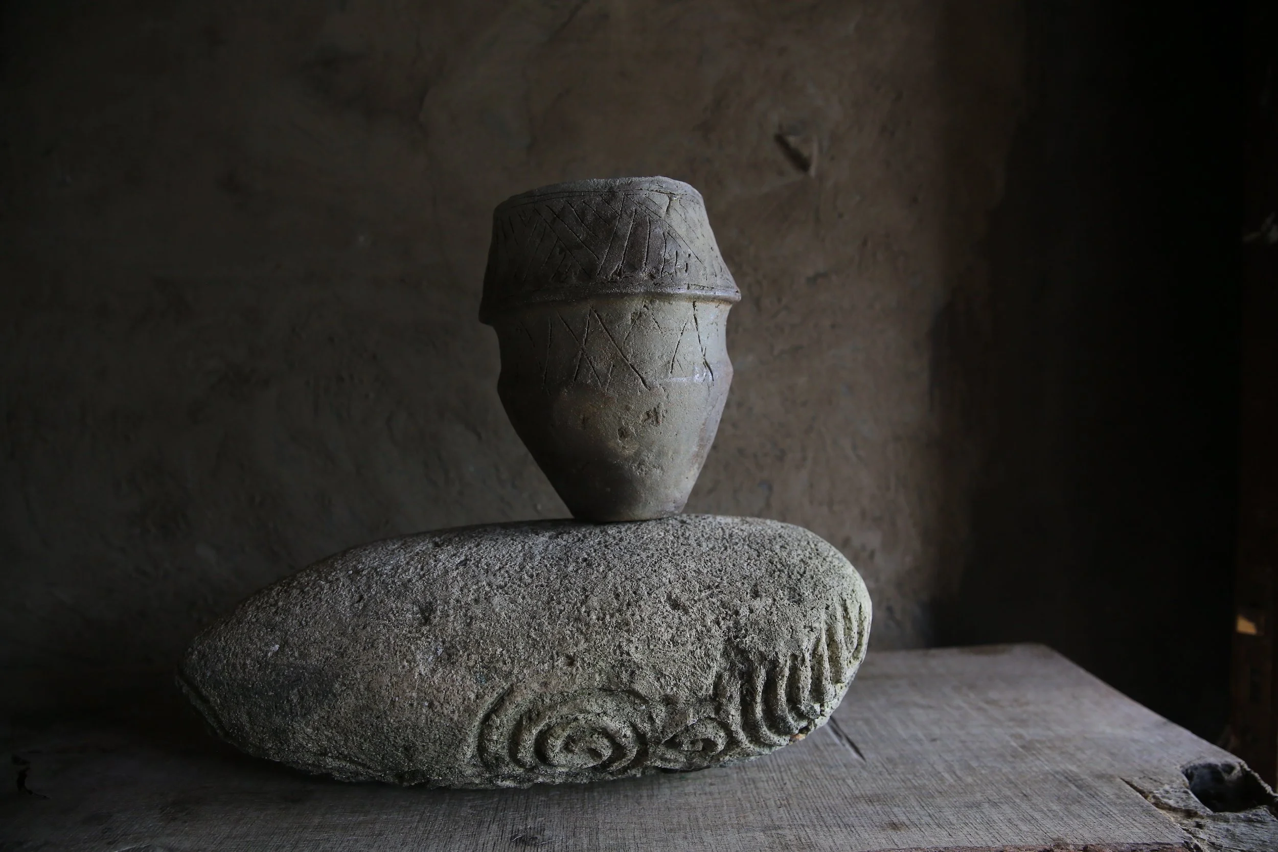 Ancient pottery vase resting on a carved stone, with a textured and dark background.