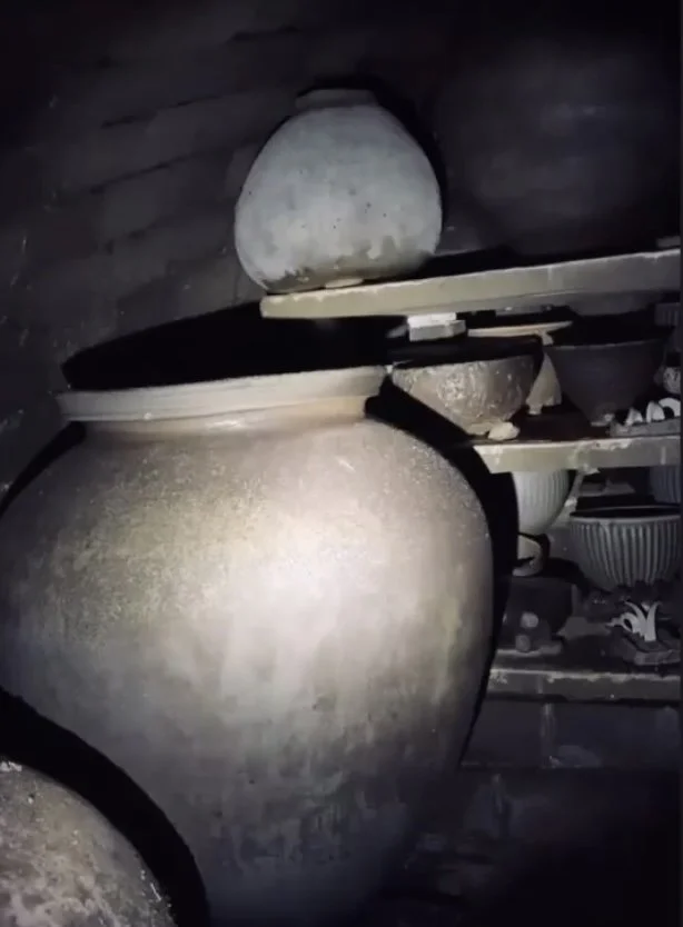 Dusty, large ceramic vases on wooden shelves in a storage space.