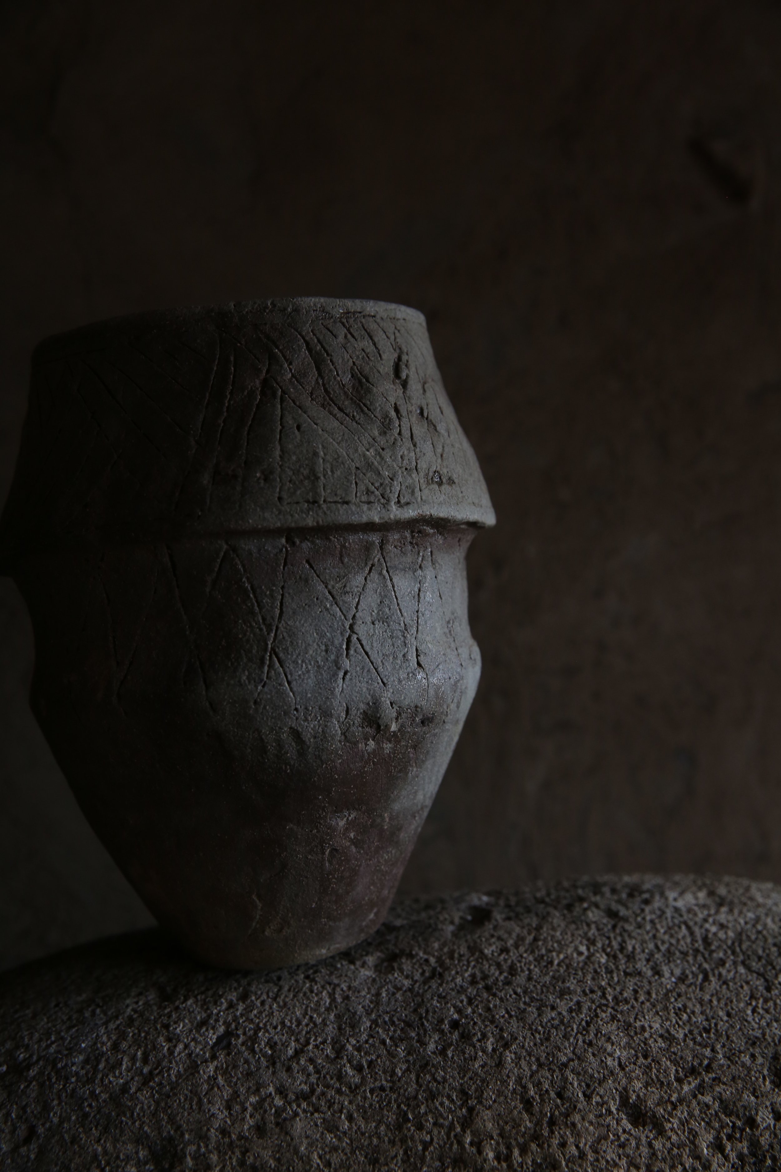 Ancient clay vessel with geometric carvings, placed on a textured surface in a dimly lit setting.