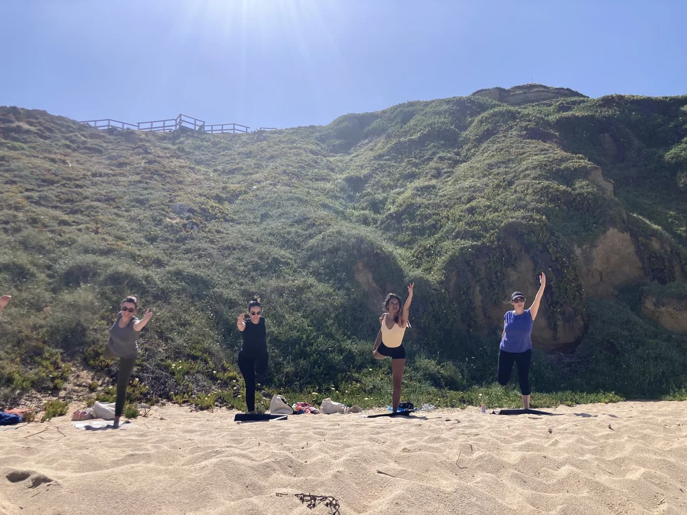 A small group practicing yoga on a beach below green cliffs near Lisbon