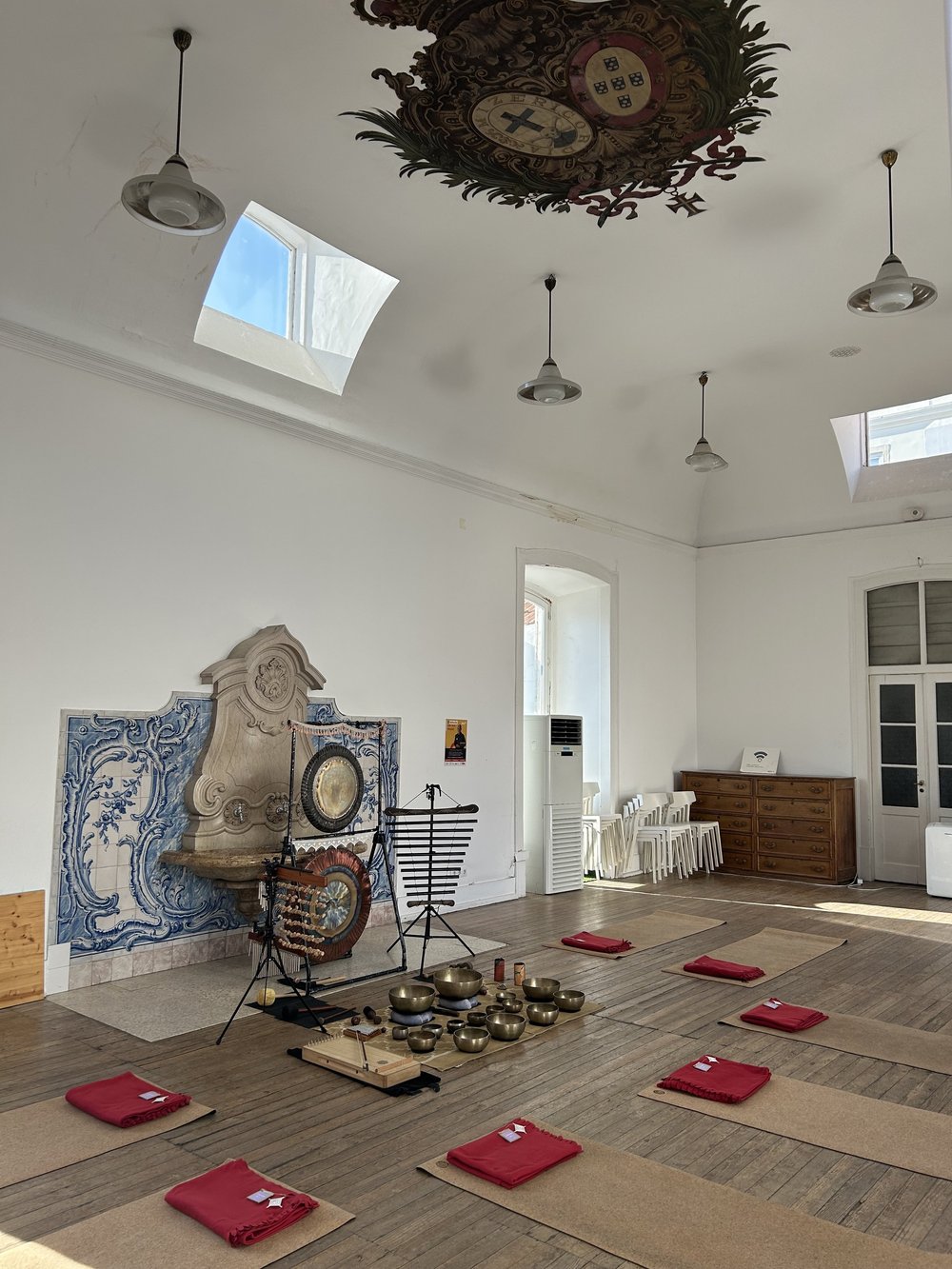 A sound bath set up with gongs, bowls and red cushions in a tiled Lisbon hall
