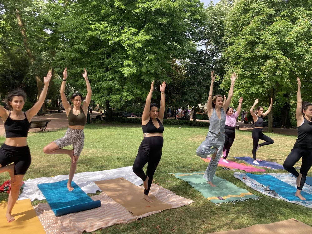 Women in tree pose on colorful mats in a green park