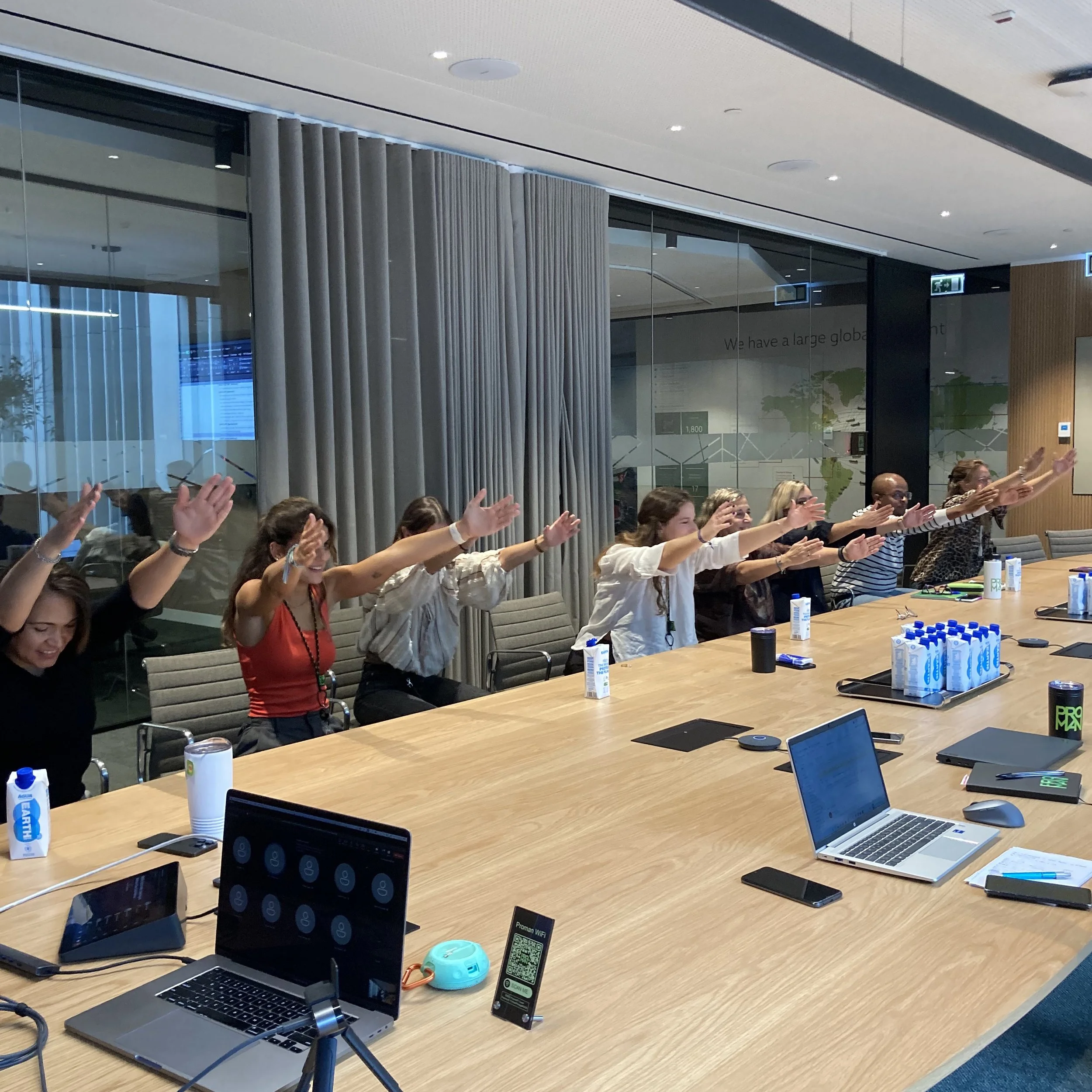 A team stretching their arms forward around a long conference table during a workplace yoga session