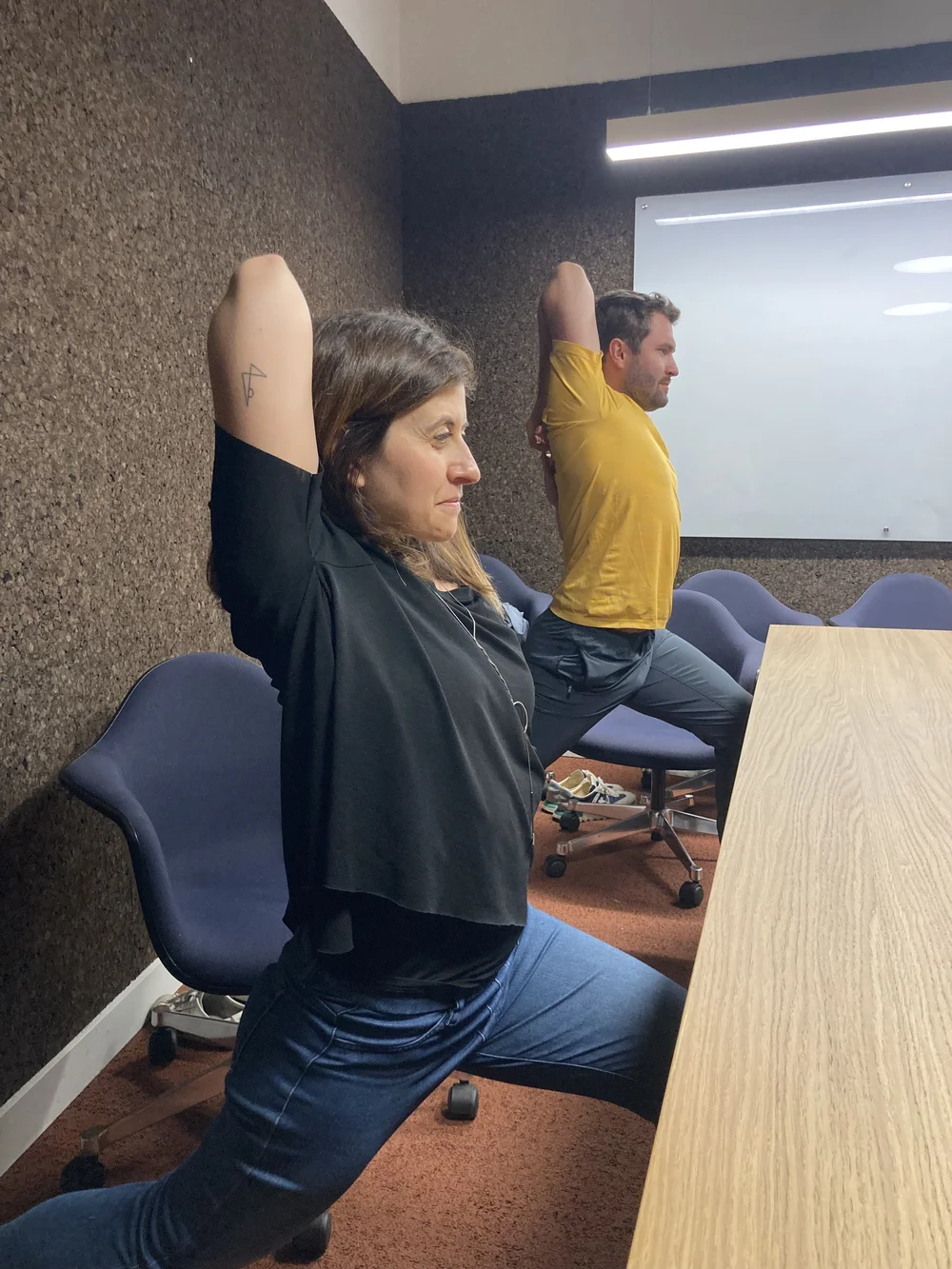 Colleagues in a low lunge stretch beside their office desk