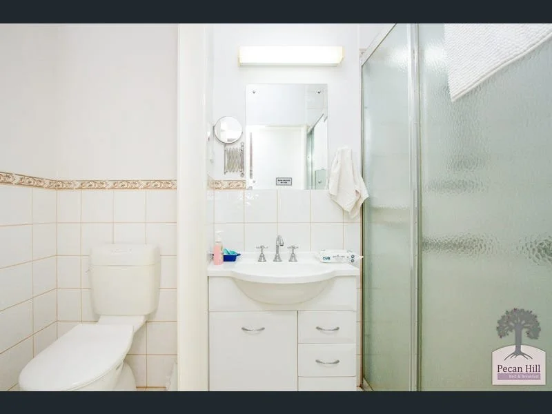 Small bathroom with a toilet, white sink with storage drawers, mirror, and a frosted glass shower door, with white tiled walls and beige decorative border.