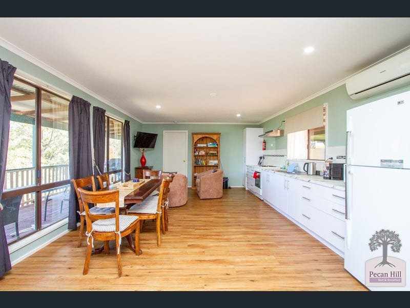 Open-plan living area with hardwood floors, large windows with dark curtains, a wooden dining table with chairs, kitchen with white cabinets, appliances, and a balcony visible outside.
