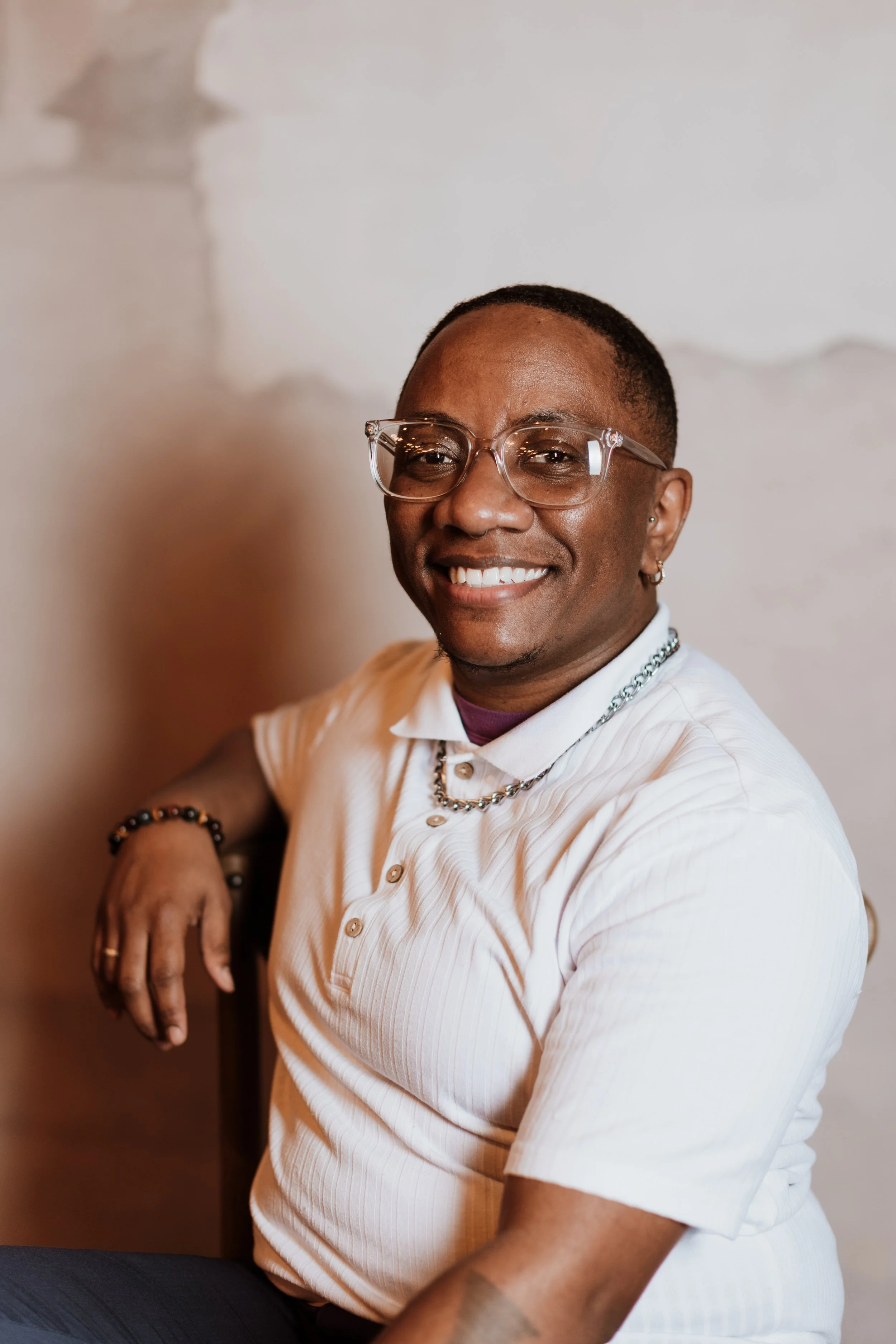 Erma Ishara, a Black person with very short hair and glasses, smiles