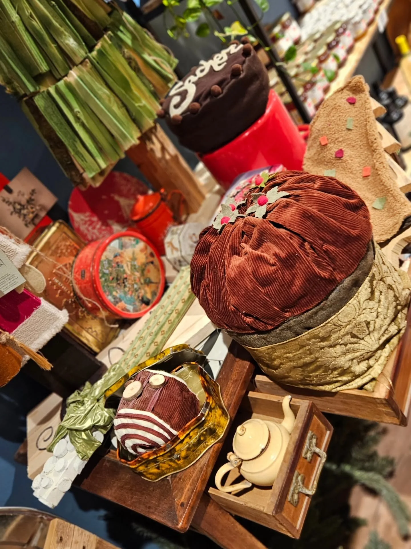 Varie decorazioni e oggetti da collezione in un mercatino, tra cui tessuti, torte finte, oggetti di ceramica e un pastore in tessuto e ovatta.