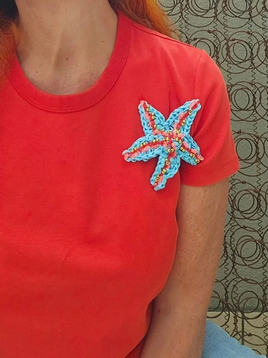 Maglietta rossa con una decorazione a forma di stella o fiore fatto di fili colorati con perline e sequins.