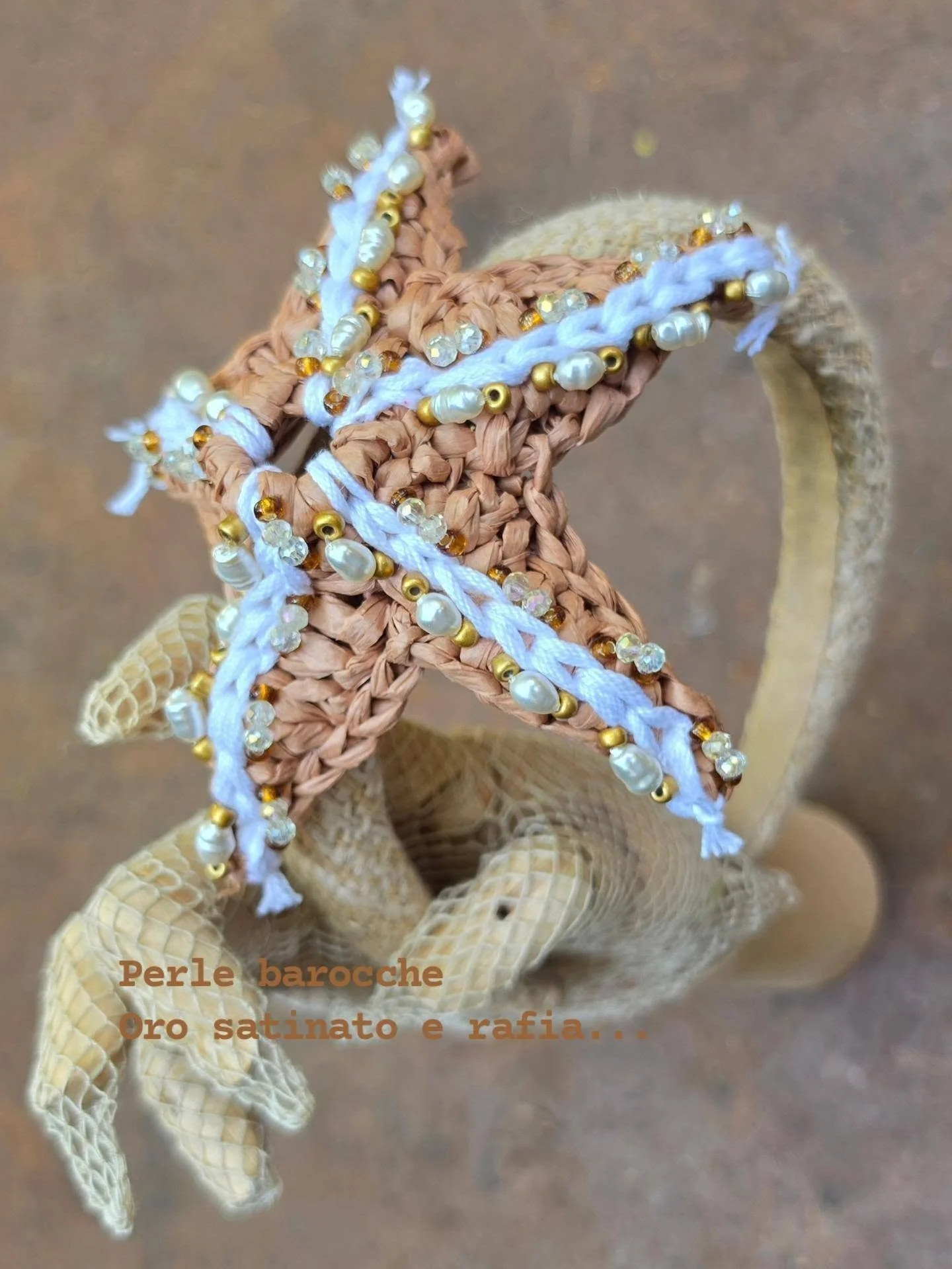 Fiocco decorato con perline barocche, perle satinate e rafia, posizionato su un supporto di sisal.