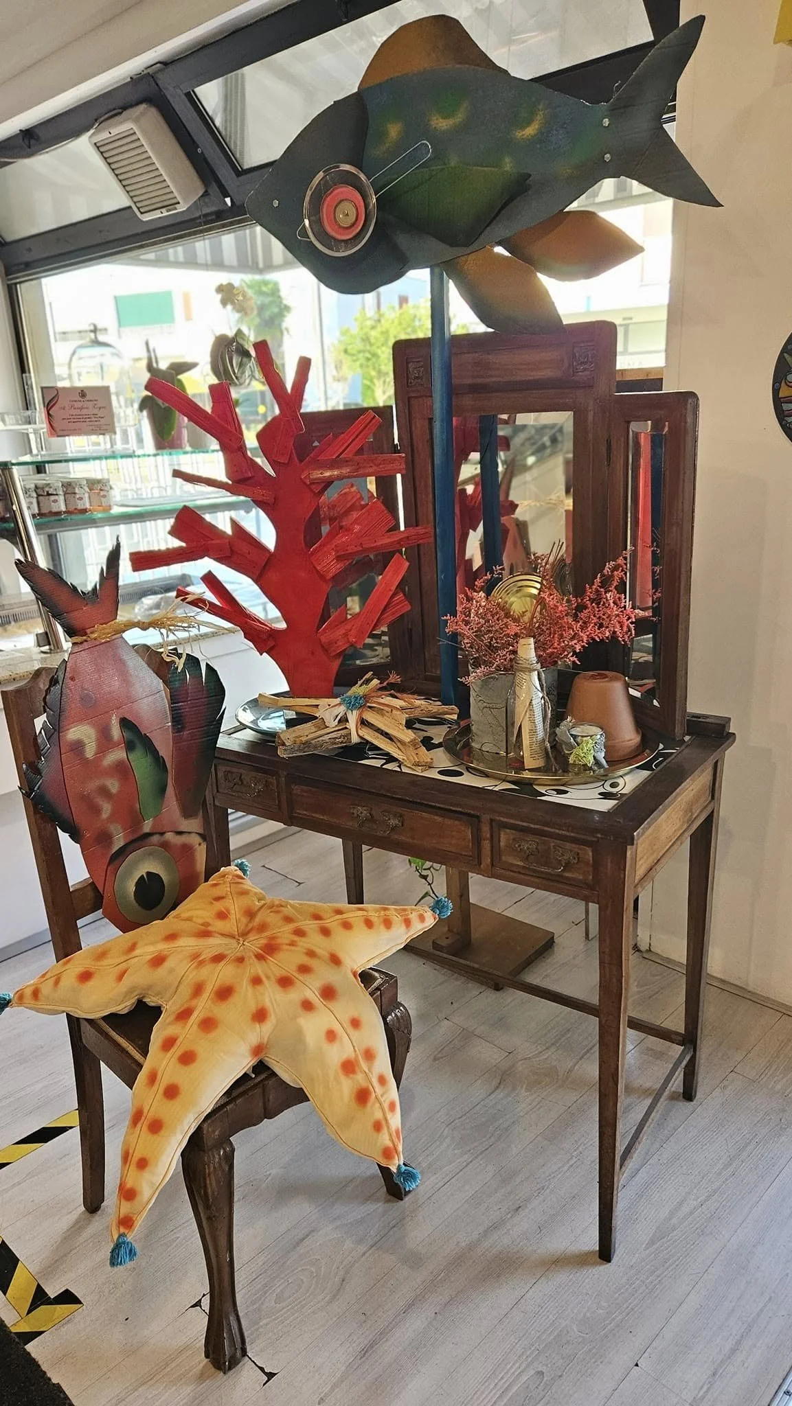 Decorazioni di legno in stile marino, come un grande pesce e un polpo di stoffa, posizionate su un tavolo in un negozio.