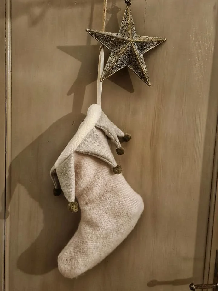 Calza natalizia bianca e cappello di Santa Claus appoggiati a una parete di legno, con una decorazione a forma di stella di Natale decorativa sopra.