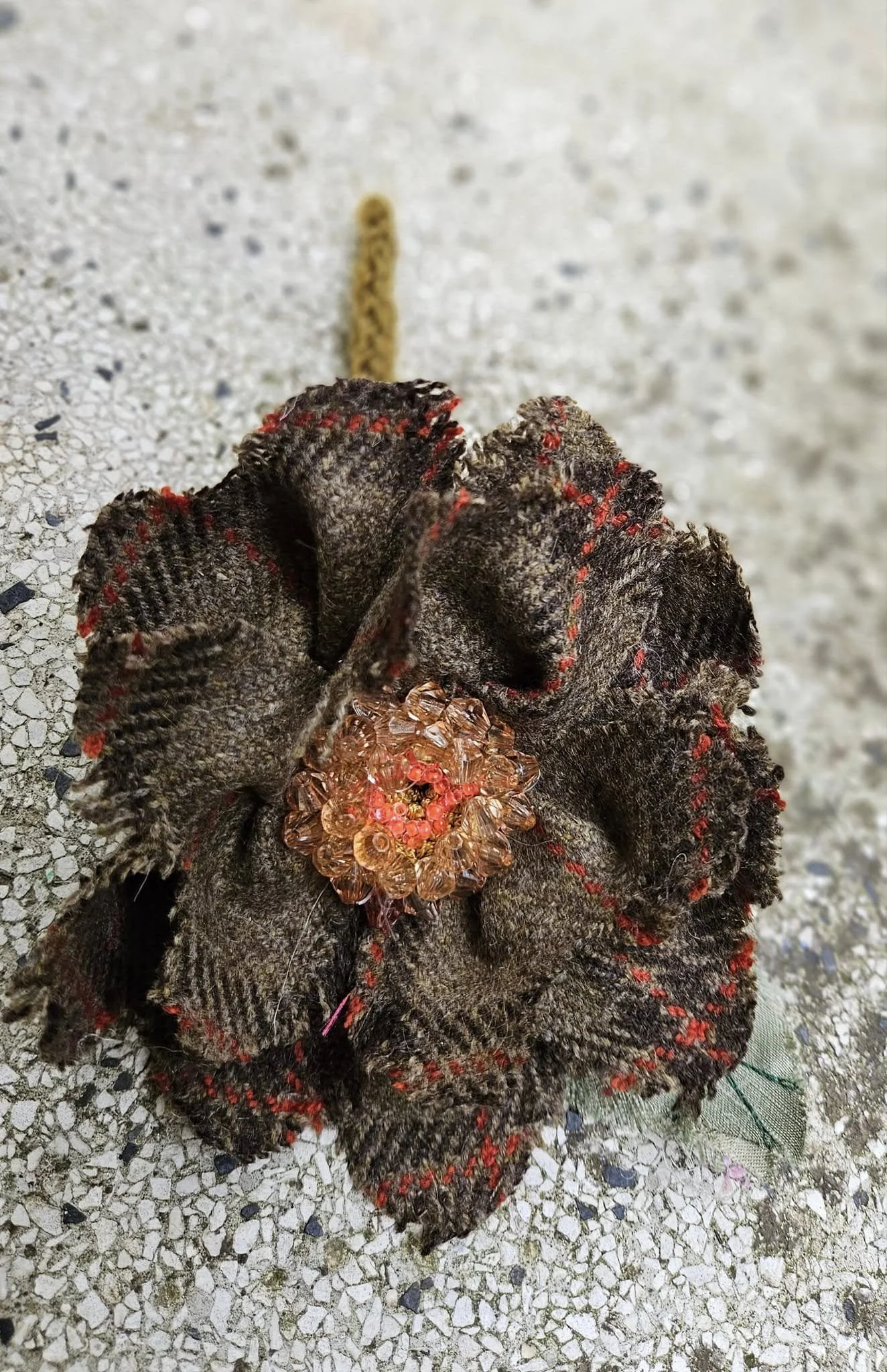 Una mano indossa un guanto di tessuto scuro con dettagli rossi, che tiene un ragno con un corpo trasparente e arancione, e uno sfondo di pavimento di pietra.