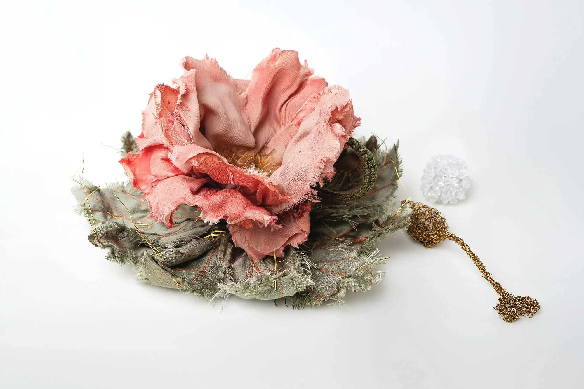 Decorazione natalizia con fiore in tessuto rosa antico, base in foglie grige e dettagli dorati e bianchi.