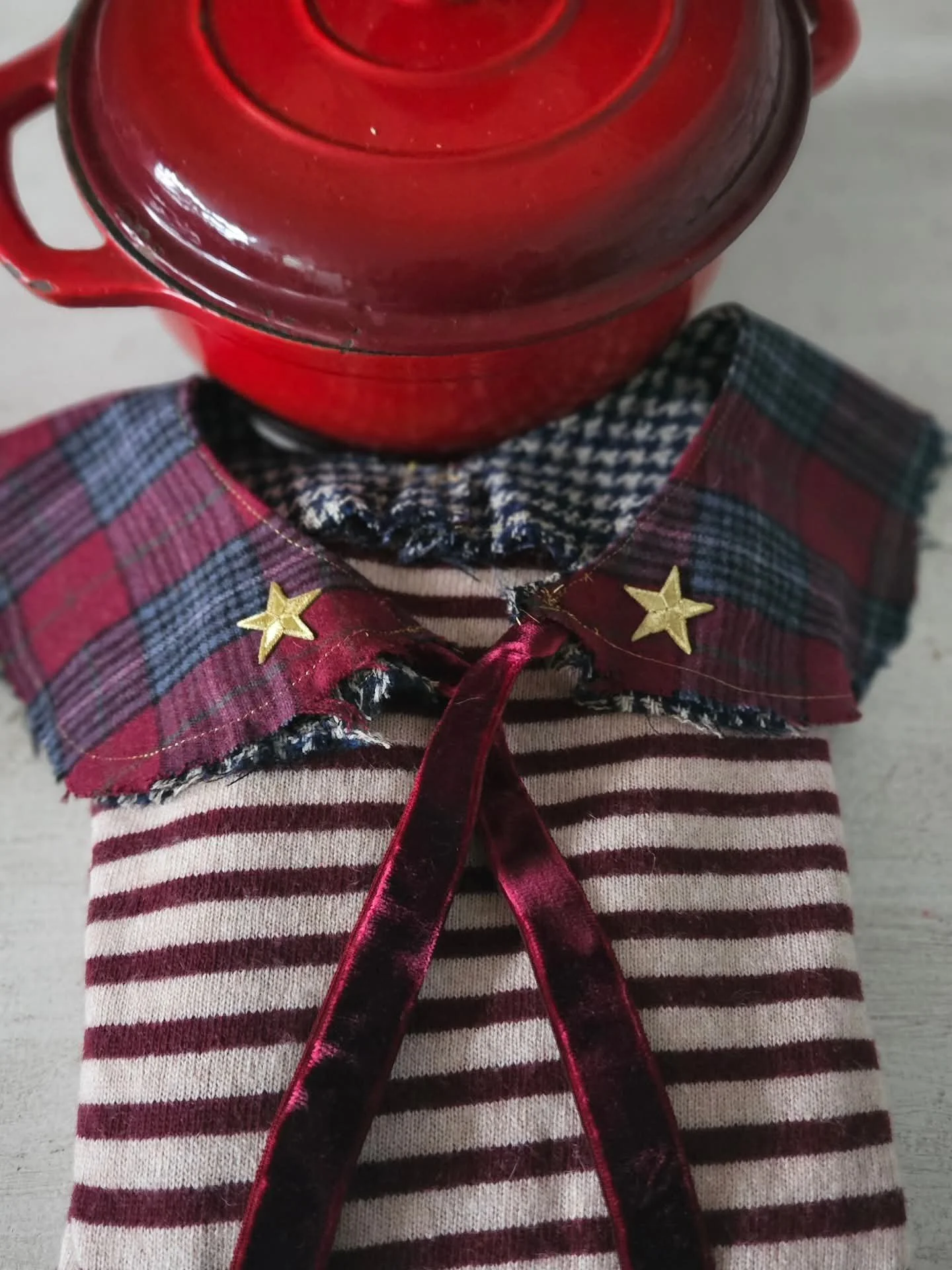 Immagine di un bambino con una giacca a righe bianco e rosse, che porta un colletto di tessuto con motivo a quadretti. Sopra la giacca, un foulard di velluto rosso con due stelle di metallo dorato fissate su di esso. Sopra la tazza rossa, una tazza di ceramica rossa.