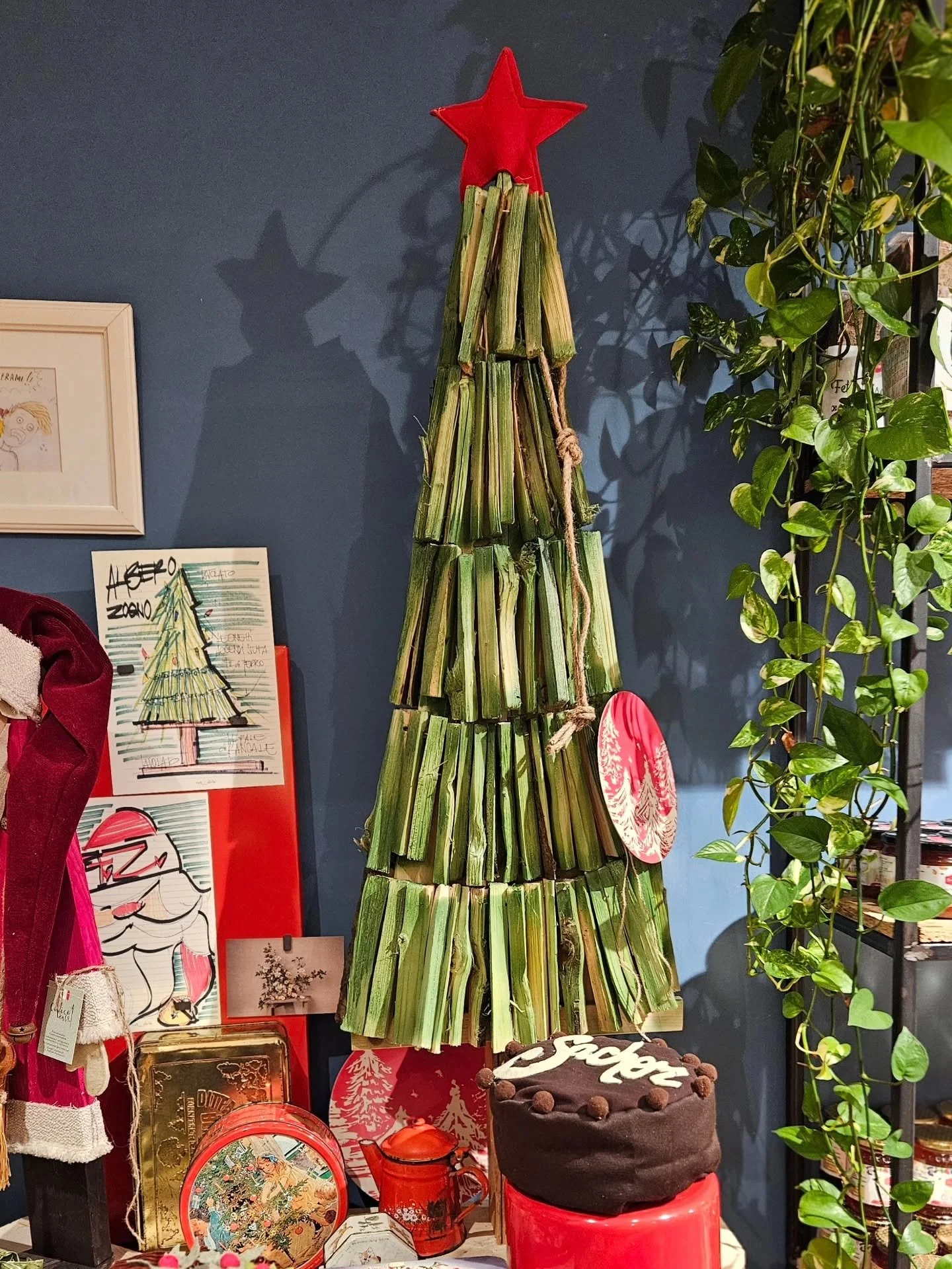 Un albero natalizio decorato con rami di sedano e una stella rossa sulla sommità, circondato da decorazioni natalizie e piante verdi.