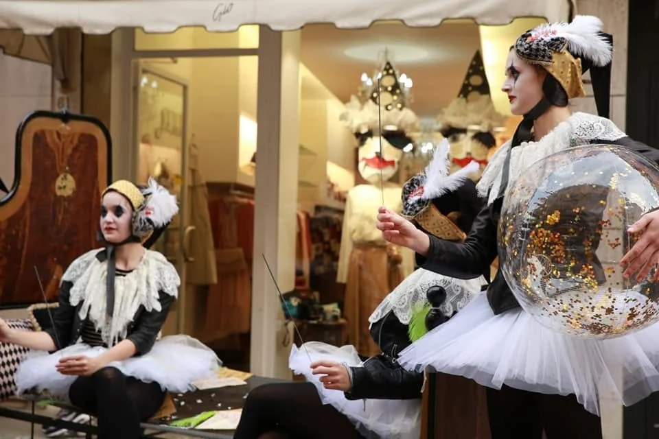 Due donne sono travestite da topini, con costumi con orecchie, tutù bianchi e dettagli dorati, e stanno facendo uno spettacolo di burattini con marionette a forma di topini.
