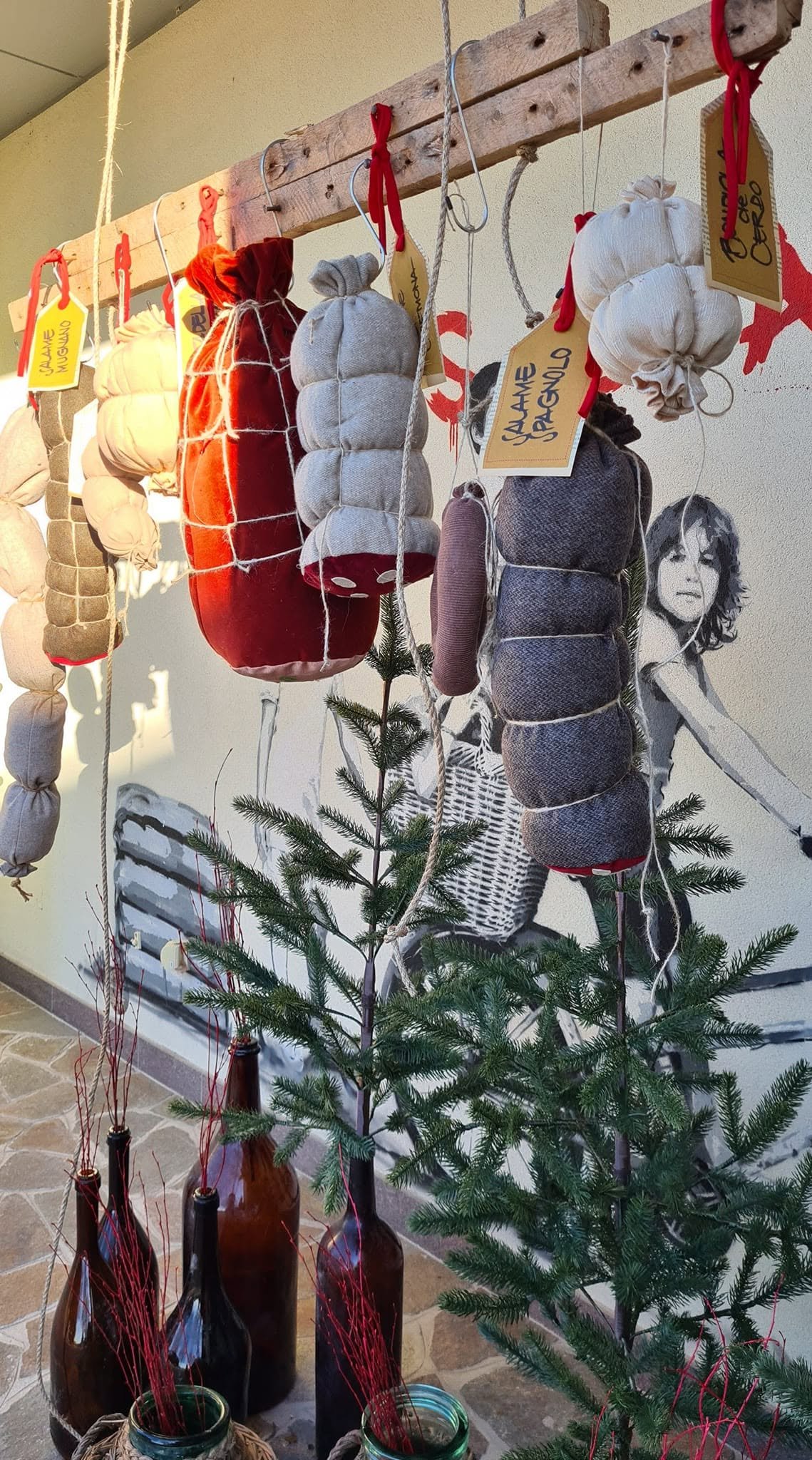 Decorazioni natalizie fatte con tessuti e corde appese a una struttura di legno, intorno a un albero di Natale.