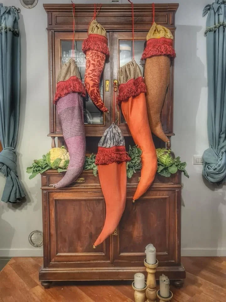 Calze natalizie grandi di stoffa colorata appese a una credenza di legno con cibo e ghirlande ornamentali sopra di Civico vent8 