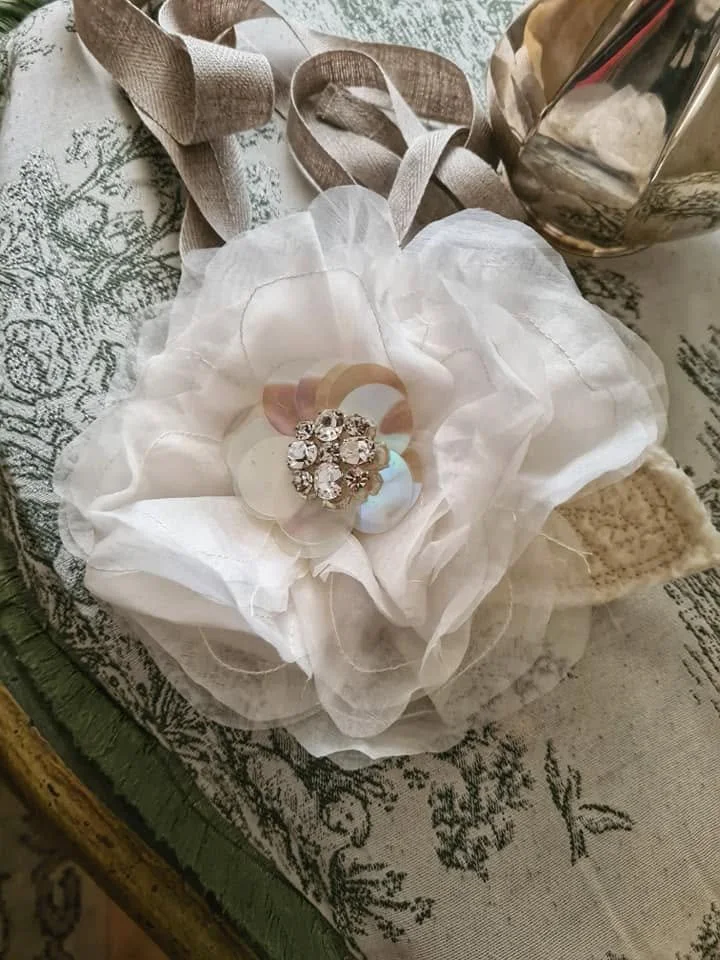 Un fiore di stoffa bianco che funge da decorazione, con al centro una composizione di strass o cristalli