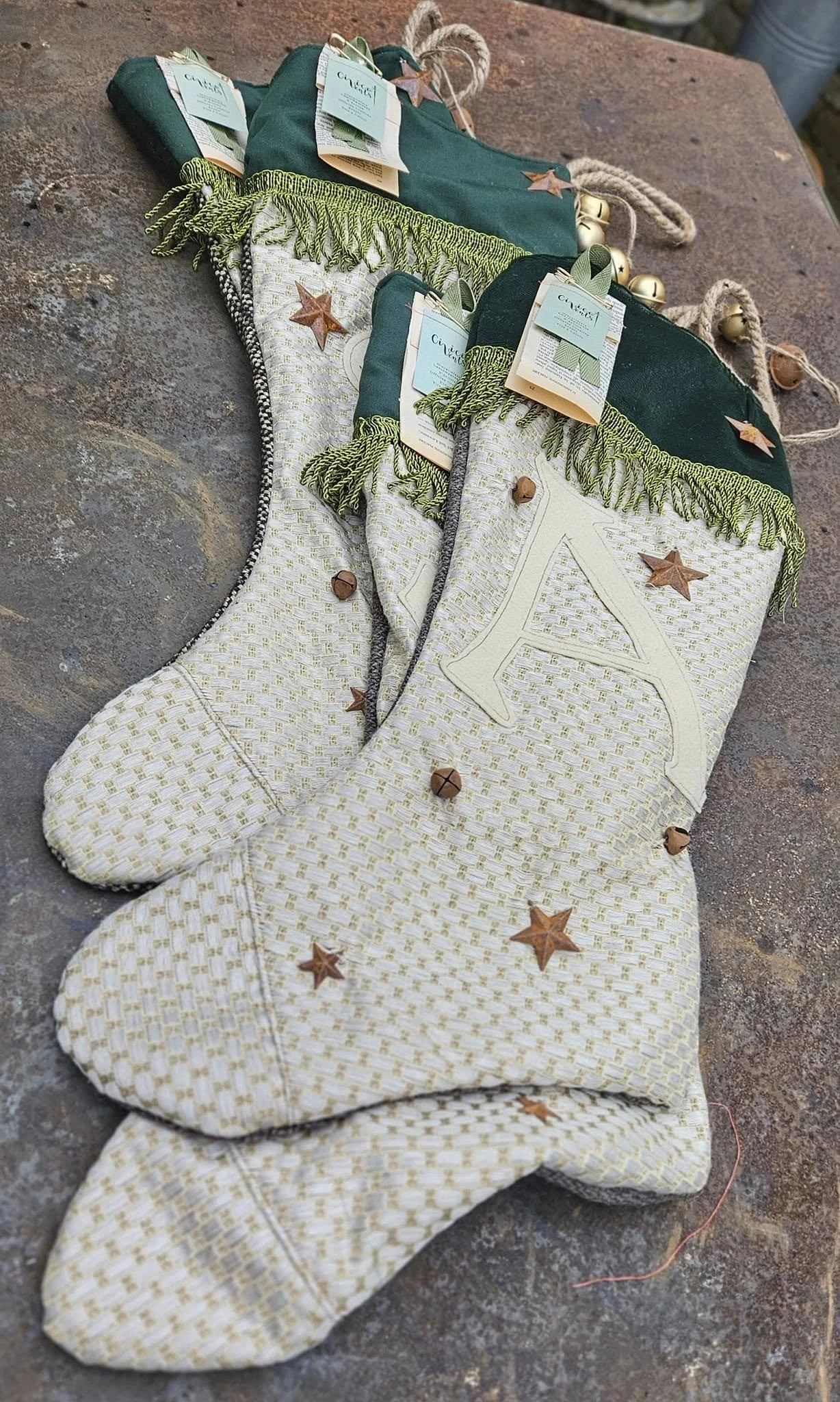 Calza natalizia decorata con stelline di legno e campanelle dorate, con etichette di stoffa blu e dettaglio di spago, stirata e posizionata su un piano di legno rustico.