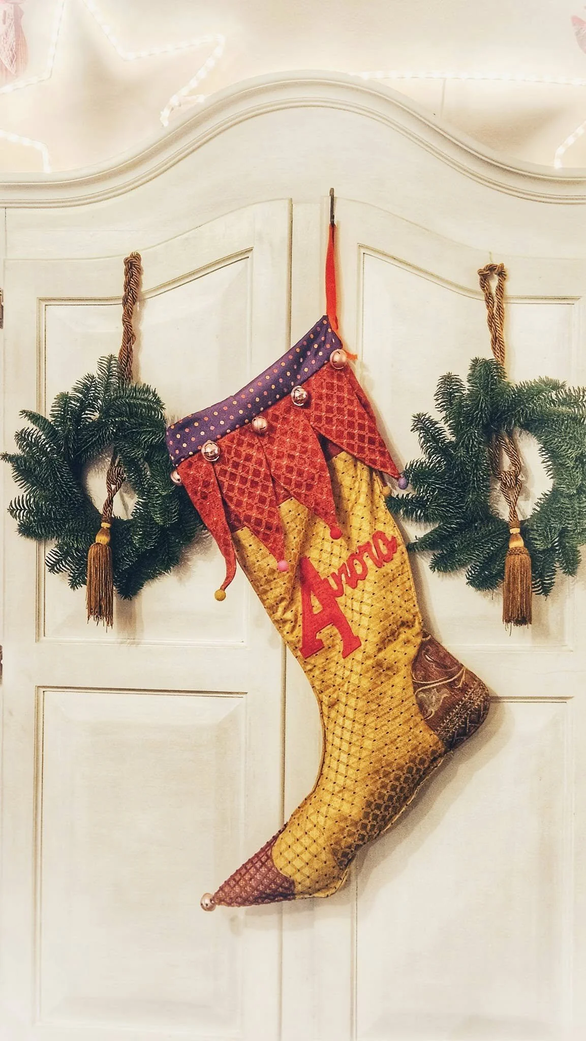 Calza natalizia decorata con nome Amy e numero 2, appesa tra due rami di abete decorativi.