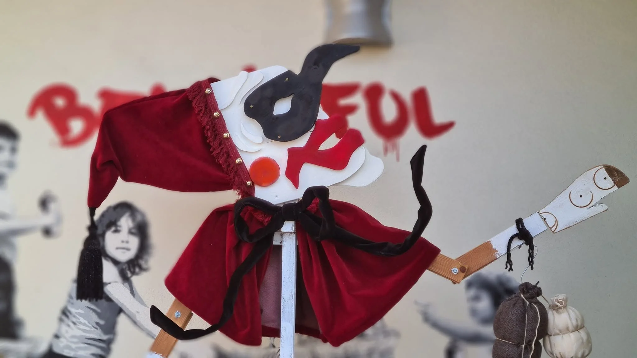 Pupazzo di burattini con vestito rosso e cappello magico, con sfondo di altre figure di burattini e disegni giapponesi.
