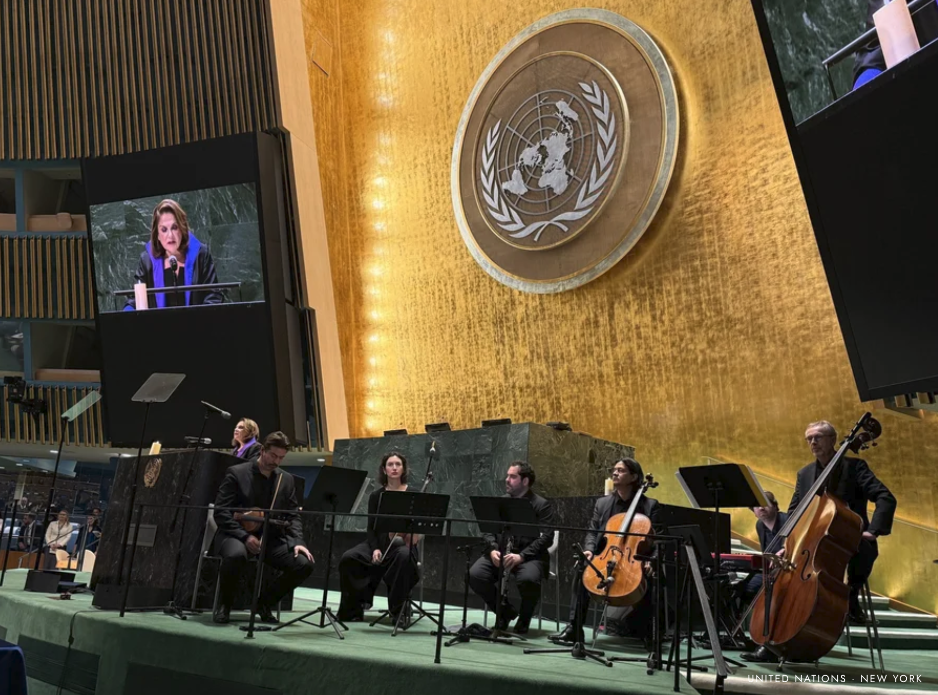 Lebensmelodien ensemble performing on stage at the United Nations headquarters in New York, with the United Nations emblem visible in the background.