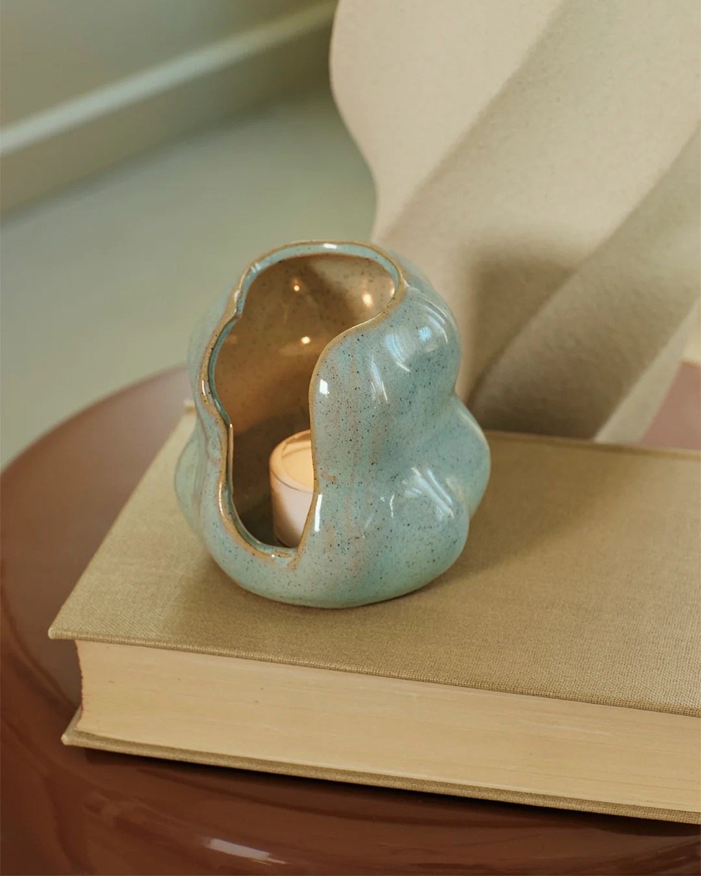 Laterne Hekla von Broste Copenhagen in Sage Green mit Teelicht auf einem beigen Buch