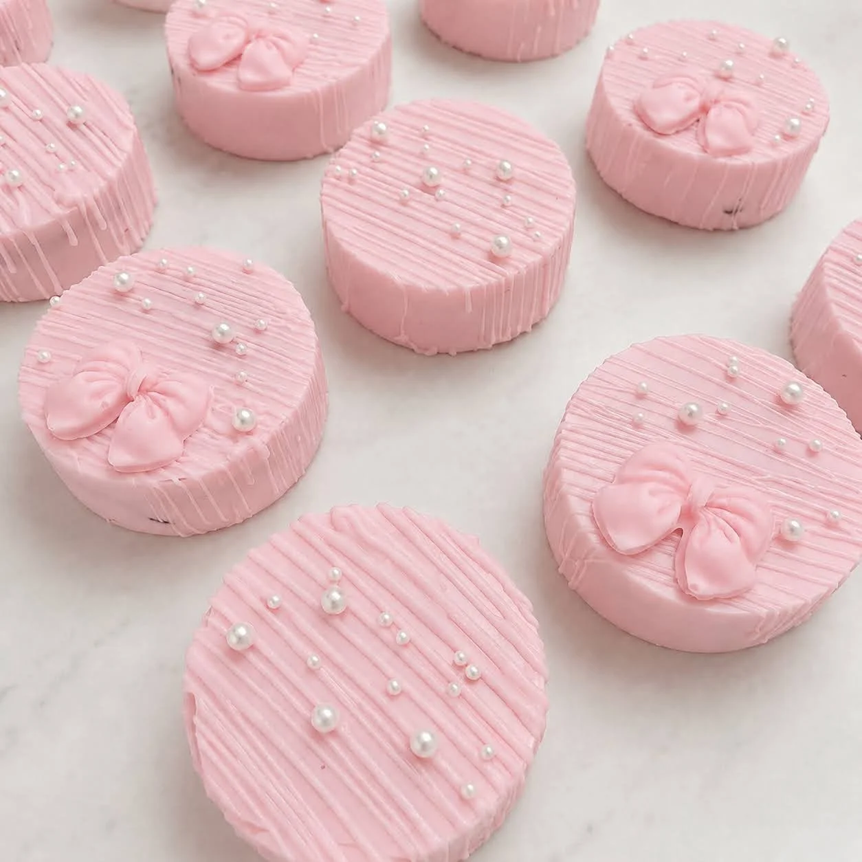 Close-up of light pink chocolate-covered Oreos decorated with fine drizzle, white sugar pearls, and pink bows.