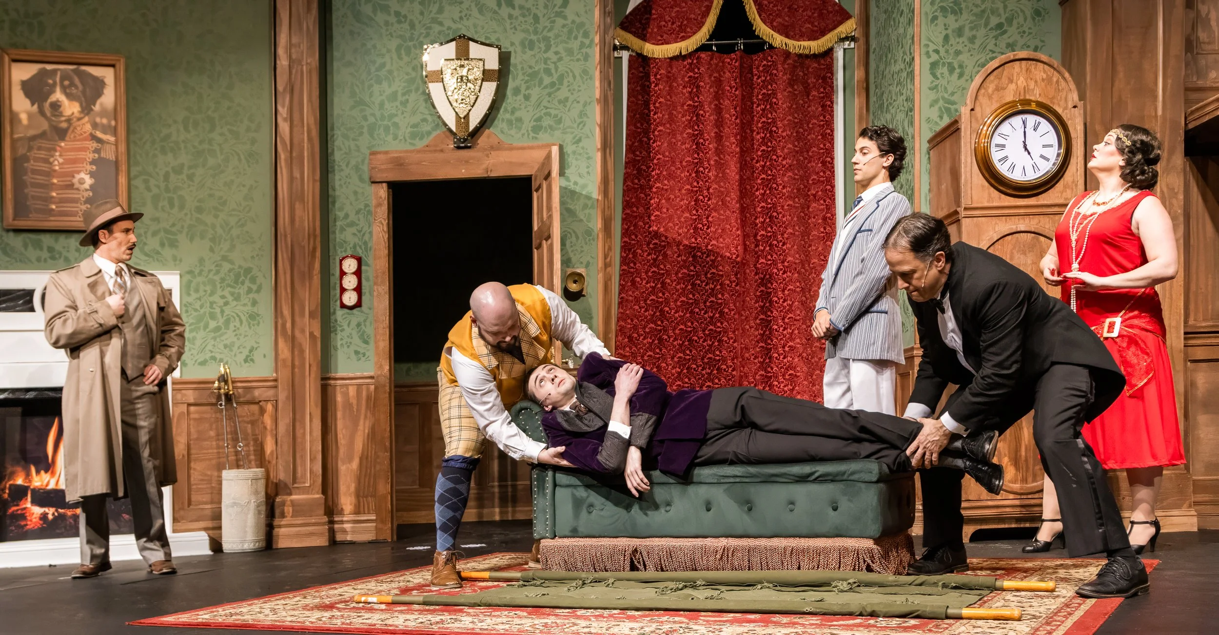 Cast of The Play That Goes Wrong in period costumes on a drawing-room set.