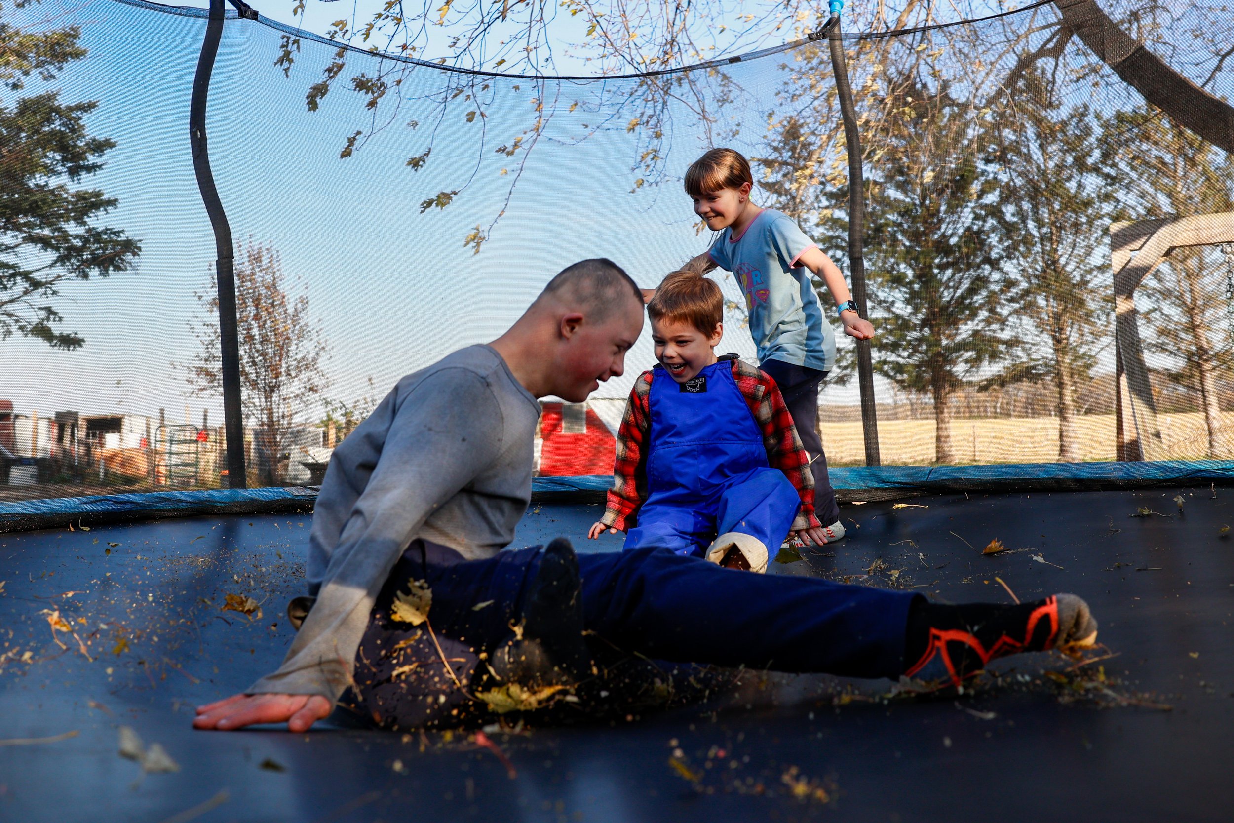 Lincoln Burman, 15, left, Anderson Shumate, 4, center, and Cathryn Burman, 11, play duck duck goose on the trampoline on Tuesday, Nov. 4, 2025, at the Burman homestead in Austin, Minn. The Burman children's mother, Shelly, has adopted 18 children, al