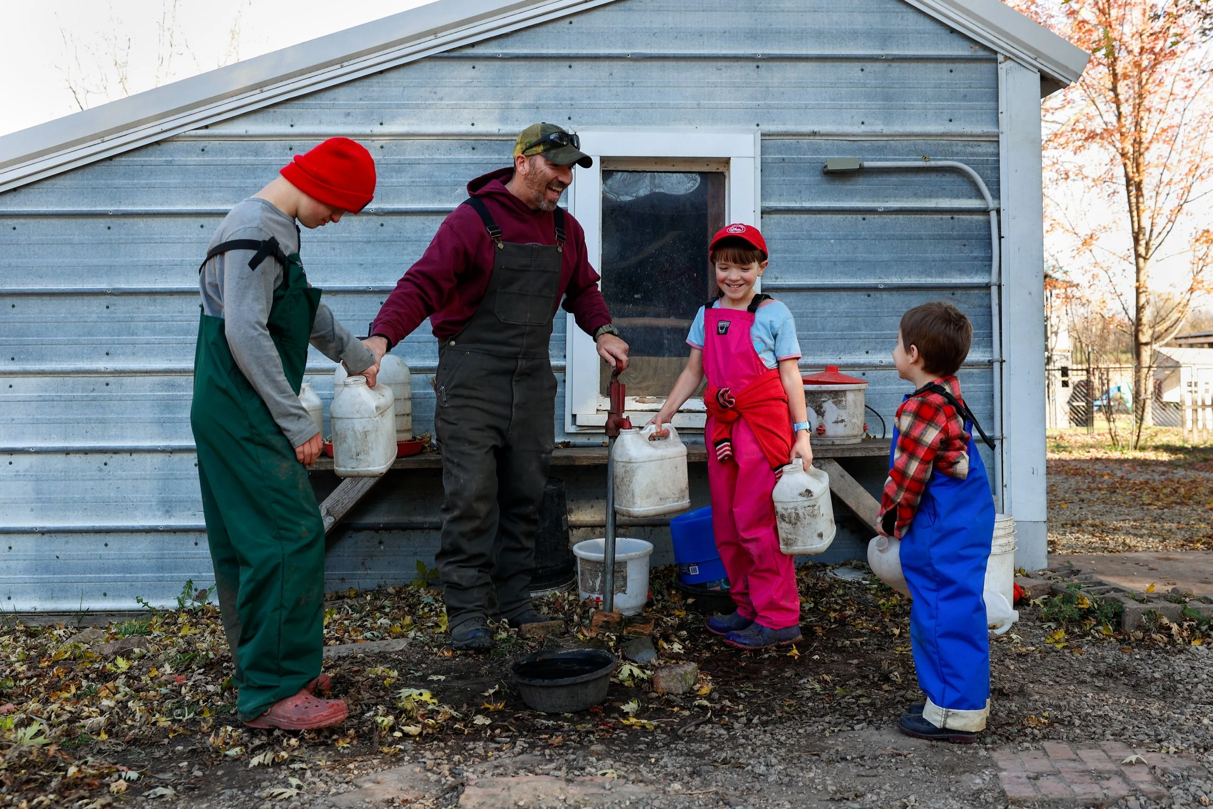 From left, Lincoln Burman, 15, Chris Shumate, Cathryn Burman, 11, and Anderson Shumate, 4, fill up water jugs to bring to the sheep on Tuesday, Nov. 4, 2025, at the Burman homestead in Austin. Chris Shumate, who previously worked with youth at a chur