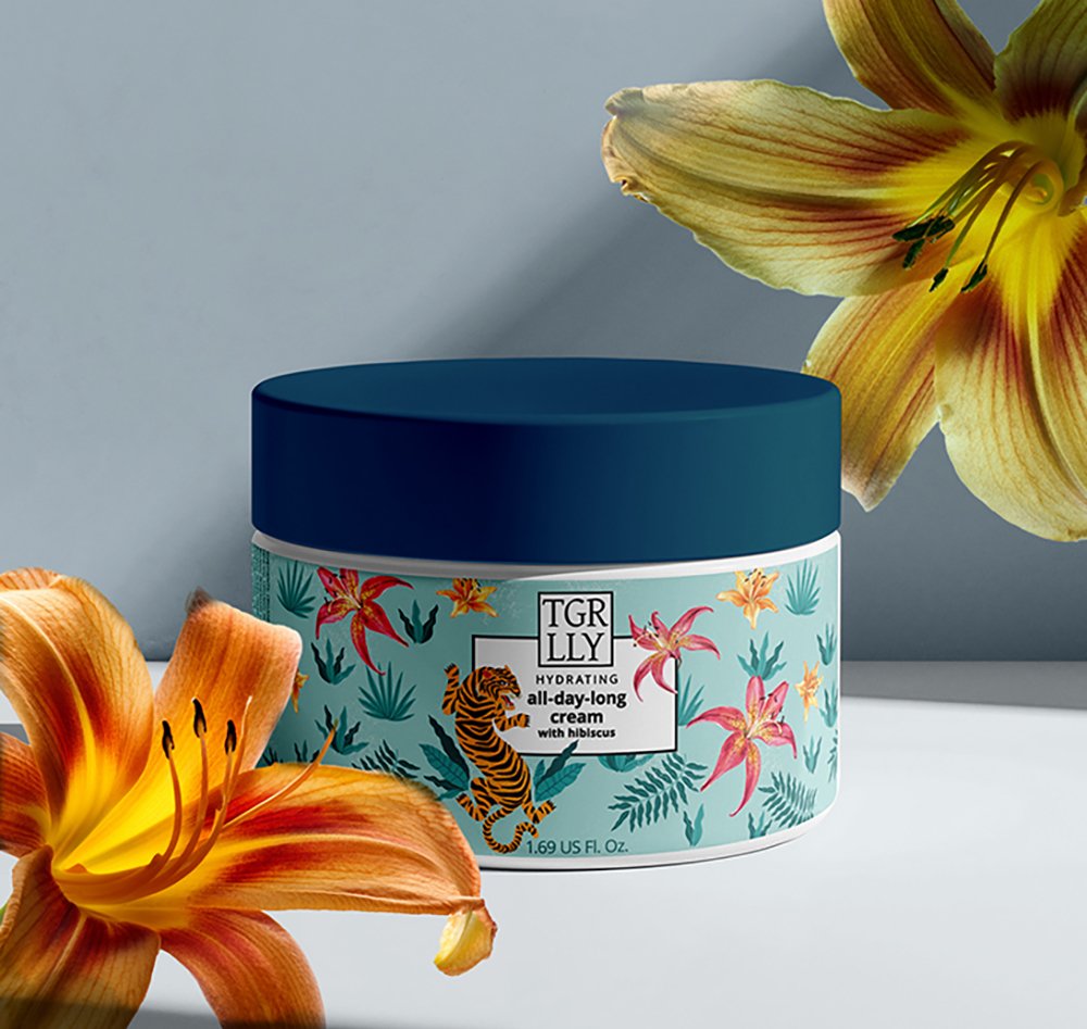 A jar of TGR LLY hydrating all-day-long cream with hibiscus surrounded by orange and yellow lilies.