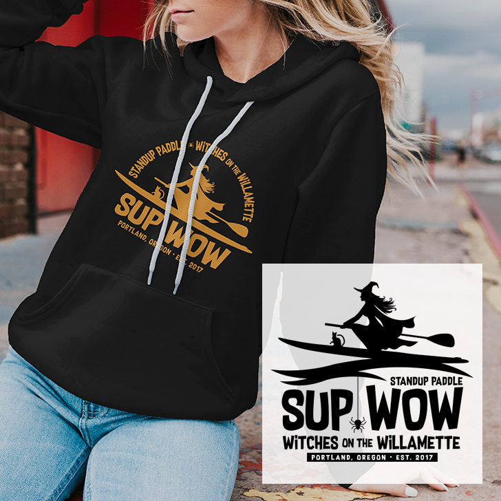 A woman wearing a black hoodie with a logo for SUP WOW, a standup paddle event for witches on the Willamette River, held in Portland, Oregon, in 2017.