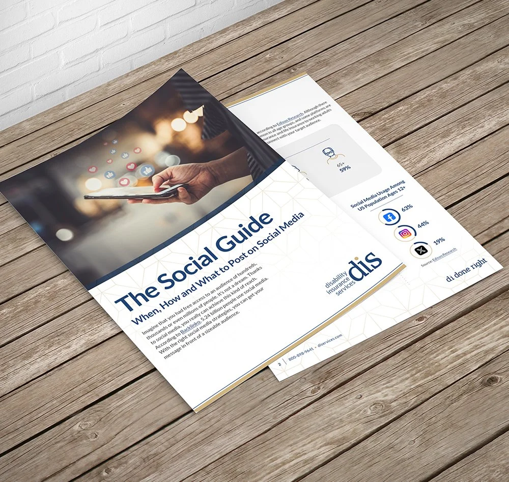 A pamphlet titled "The Social Guide" with a subtitle "When, How and What to Post on Social Media" lies on a wooden table. The pamphlet features an image of a hand holding a smartphone with social media icons floating above it.