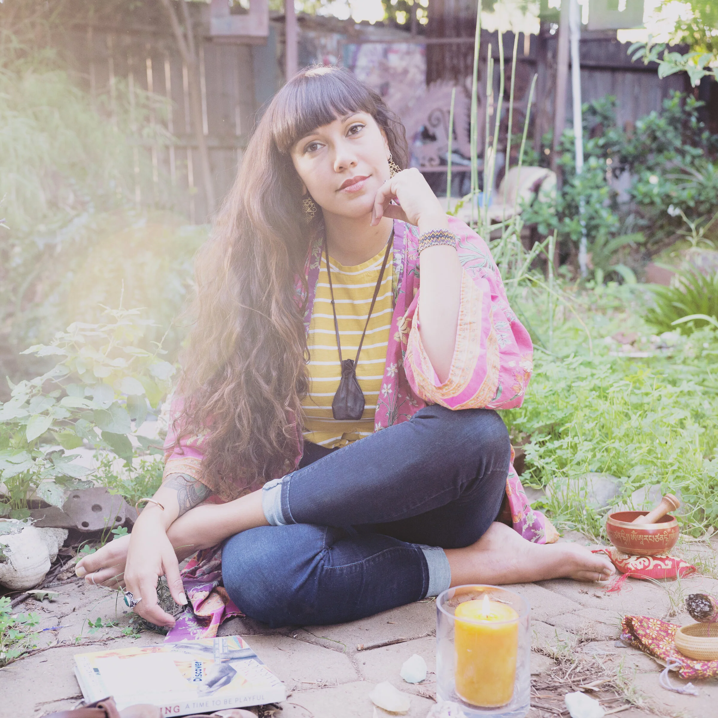 photo of isabel sitting on the ground, serene facial expression, green foliage in background