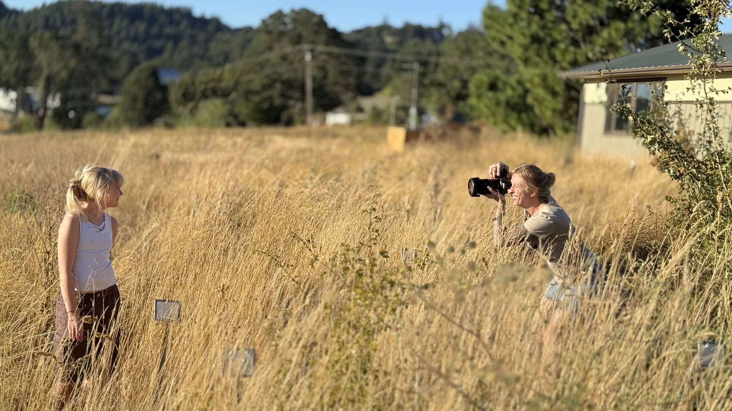 image of woman taking a photo of a girl in a field of tall dry grass
