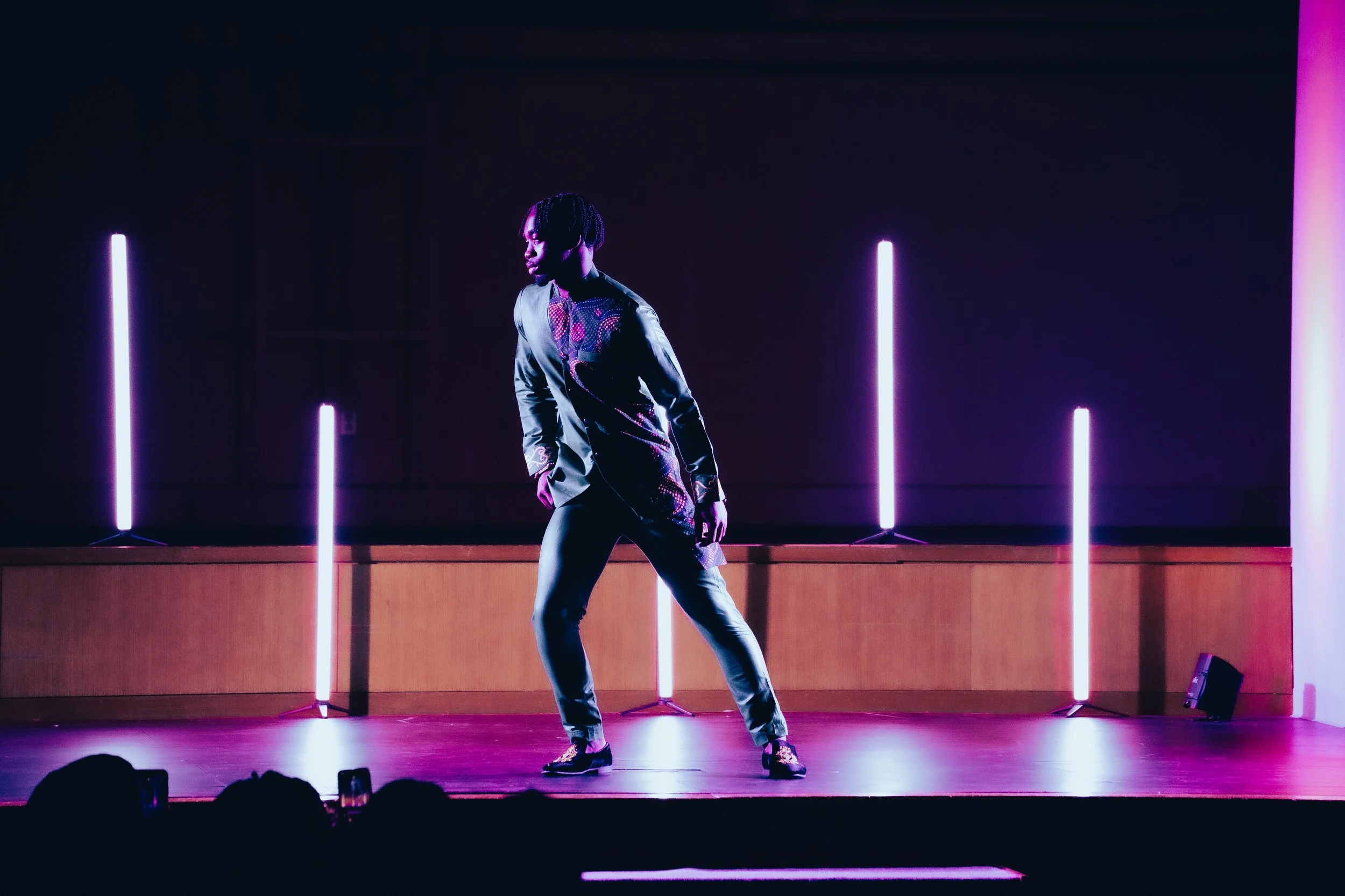 Person dancing on stage with purple and pink neon lights behind, audience visible at bottom