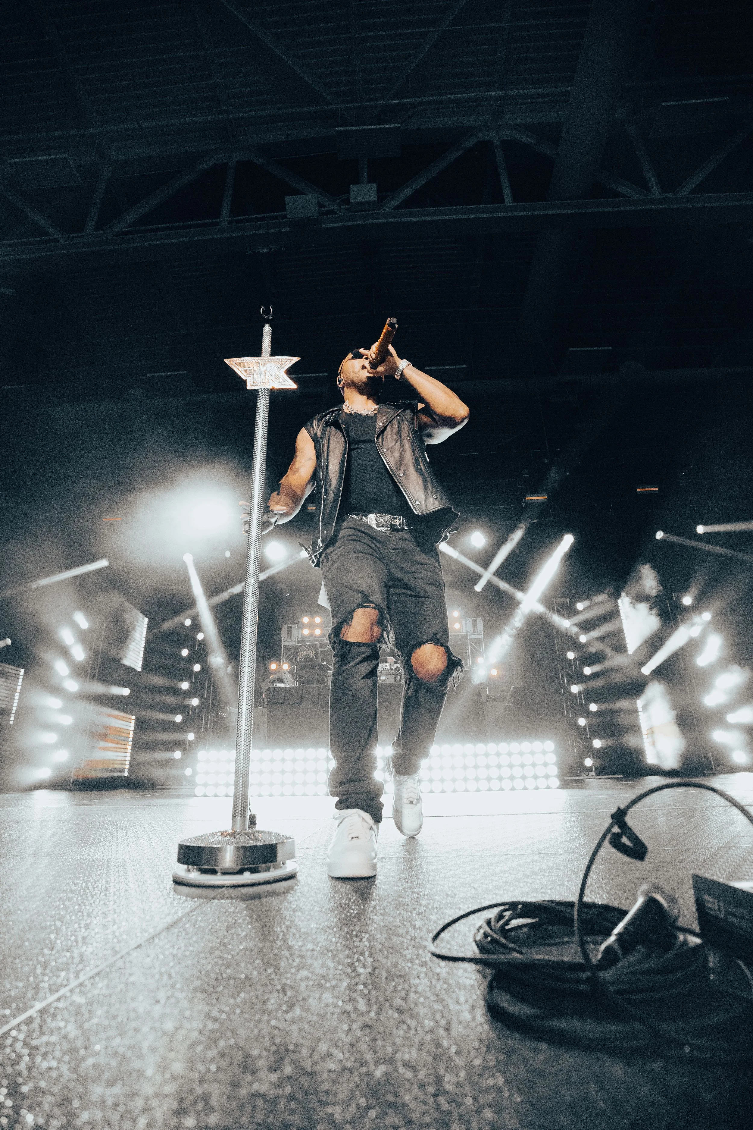 Flo-Rida singing into microphone on stage with bright lights and sound equipment.
