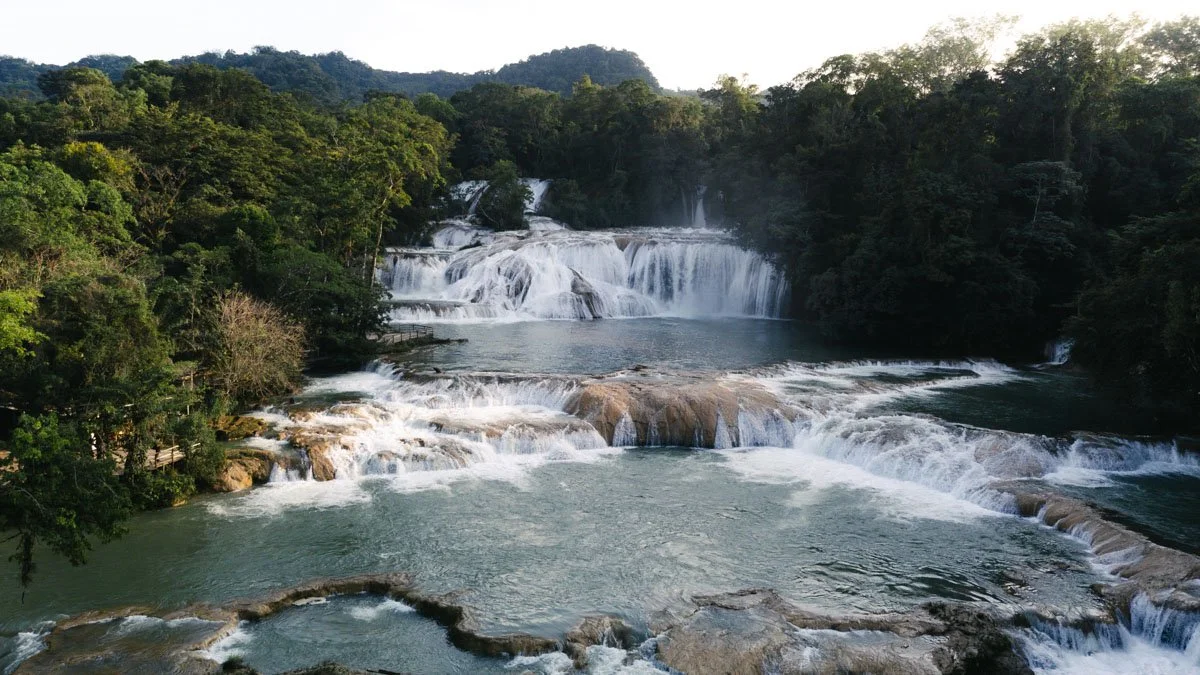 Multiple waterfalls cascading over rocks surrounded by dense green forest with hills in the background. Agua Azul, Chiapas, Mexico. Travel photography by Sergio Gutiérrez sergiogutierrezphoto.