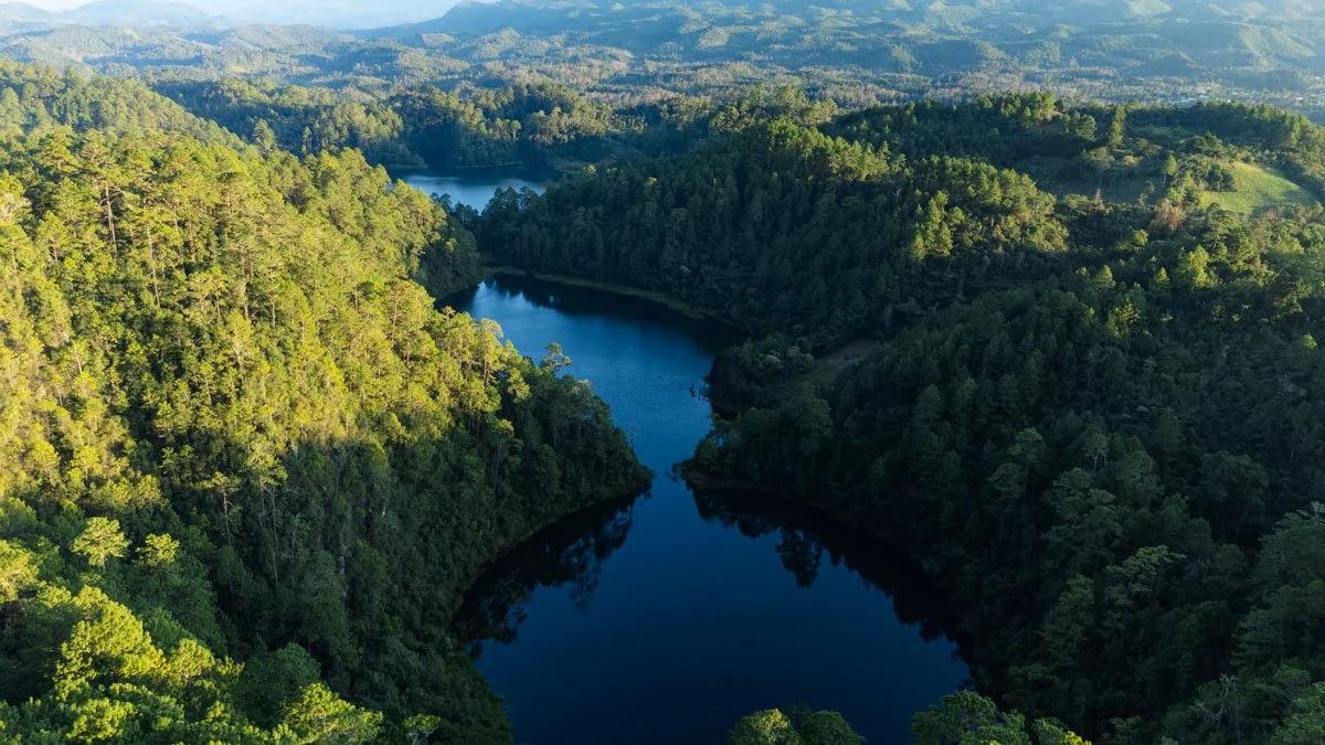 Aerial view of a winding river surrounded by lush green forested hills and distant mountains in the background. drone photography in lagunas de montebello chiapas mexico.