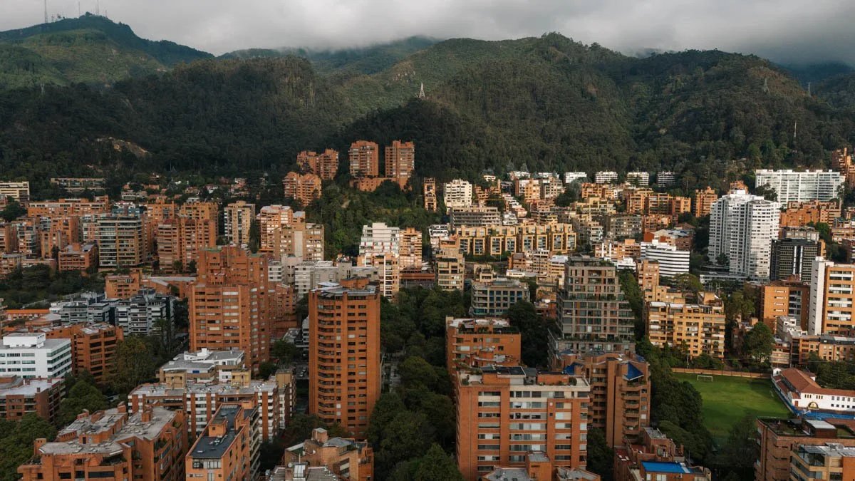 Cityscape of a densely populated urban area surrounded by green hills and mountains, with residential and commercial buildings in shades of brown, white, and gray. Bogota Colombia Travel Drone Photography by Sergio Gutiérrez sergiogutierrezphoto.