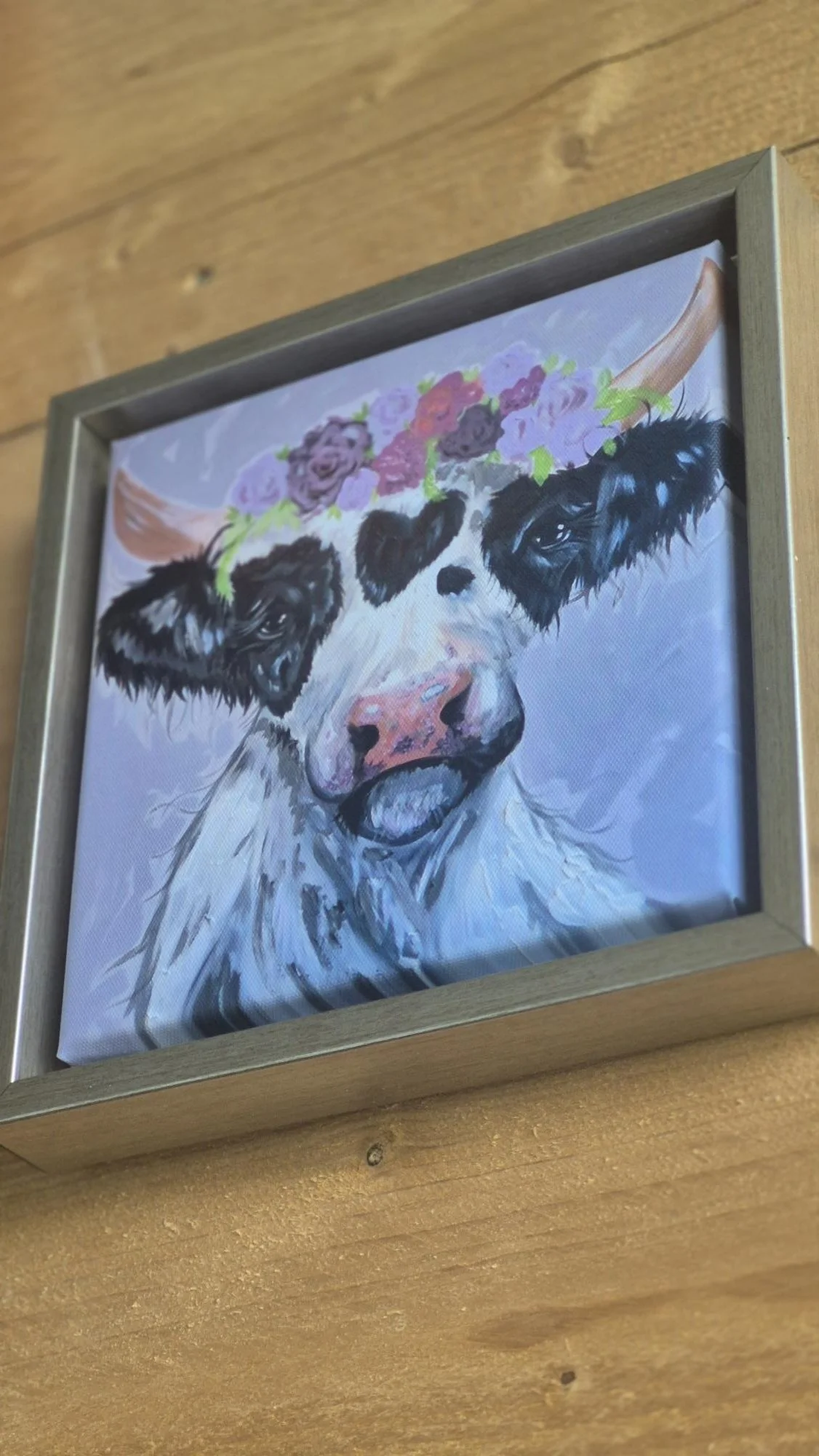 Whimsical framed canvas featuring a black and white cow with a floral crown of pink and purple flowers, rustic animal wall art decor