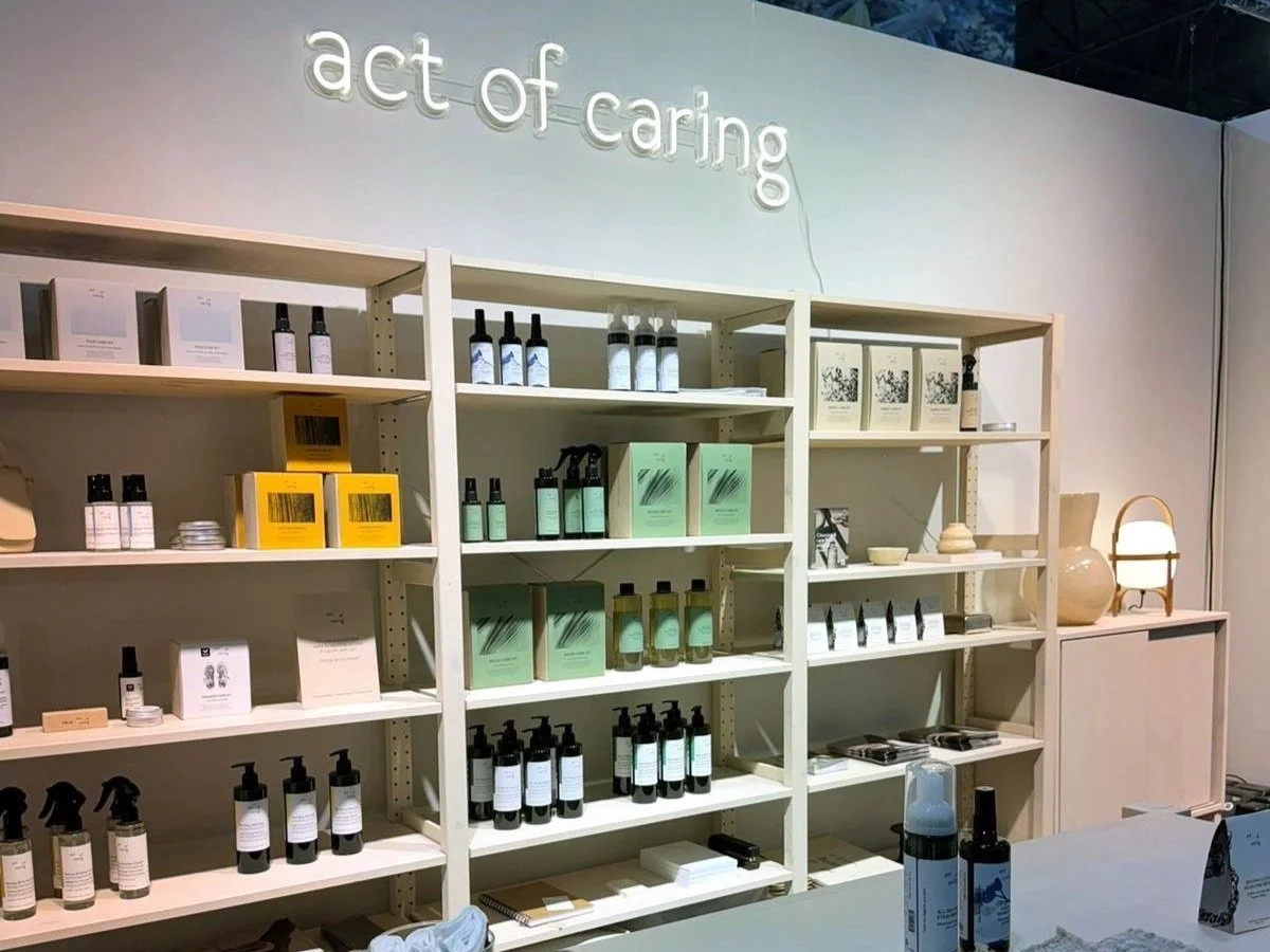 Retail display shelves holding various skincare and beauty products, boxes, and small jars, with a neon sign reading "act of caring" above.